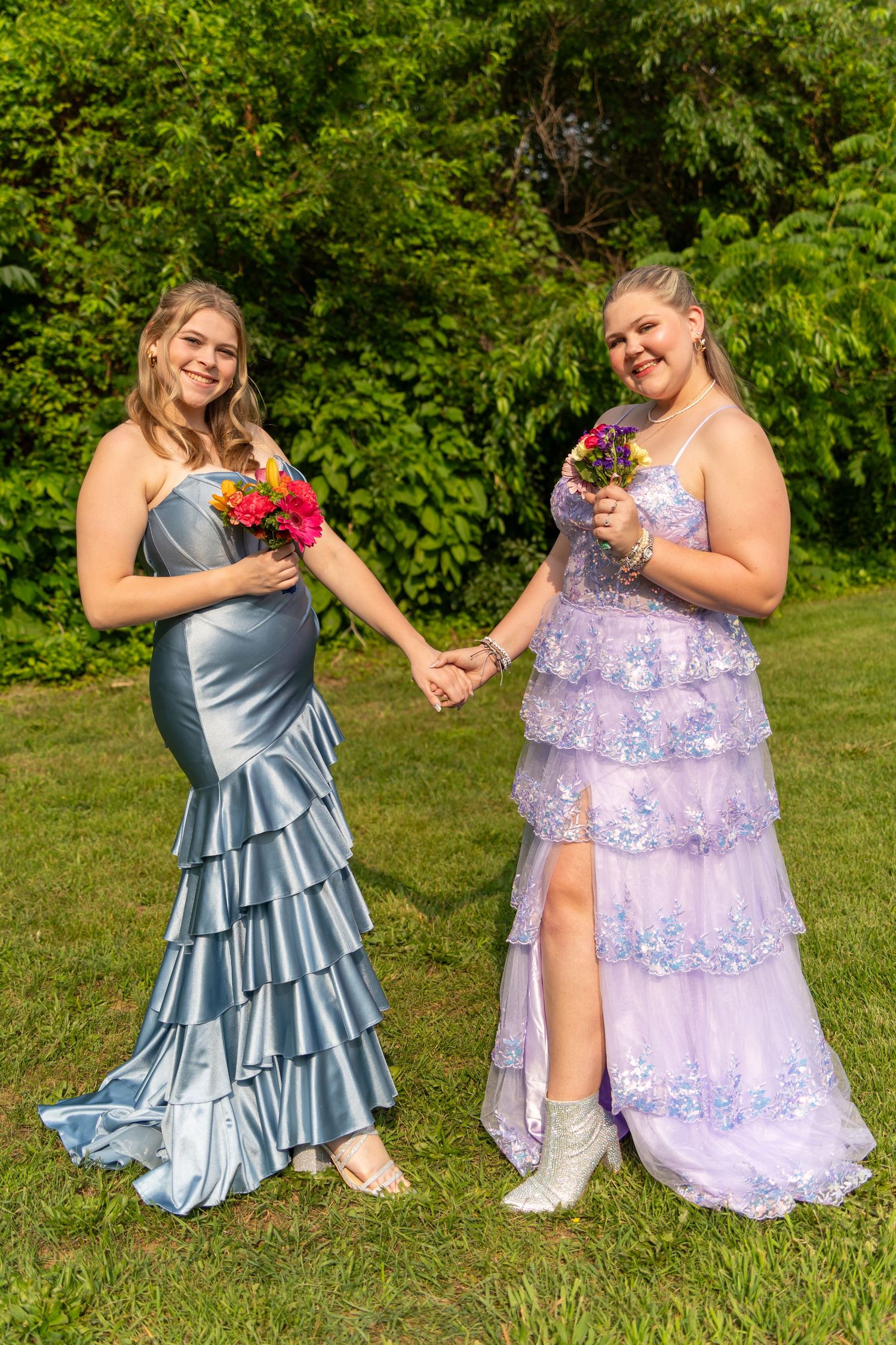 Two friends in elegant dresses perform choreographed dance moves on a sunny lawn.