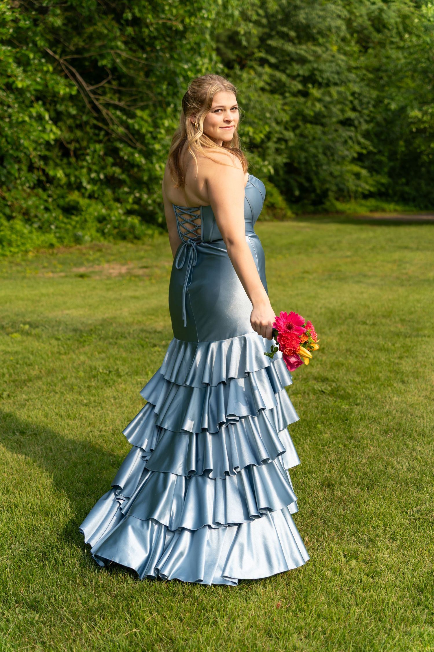 A formal portrait in a blue ruffled gown while holding red flowers in a garden setting.