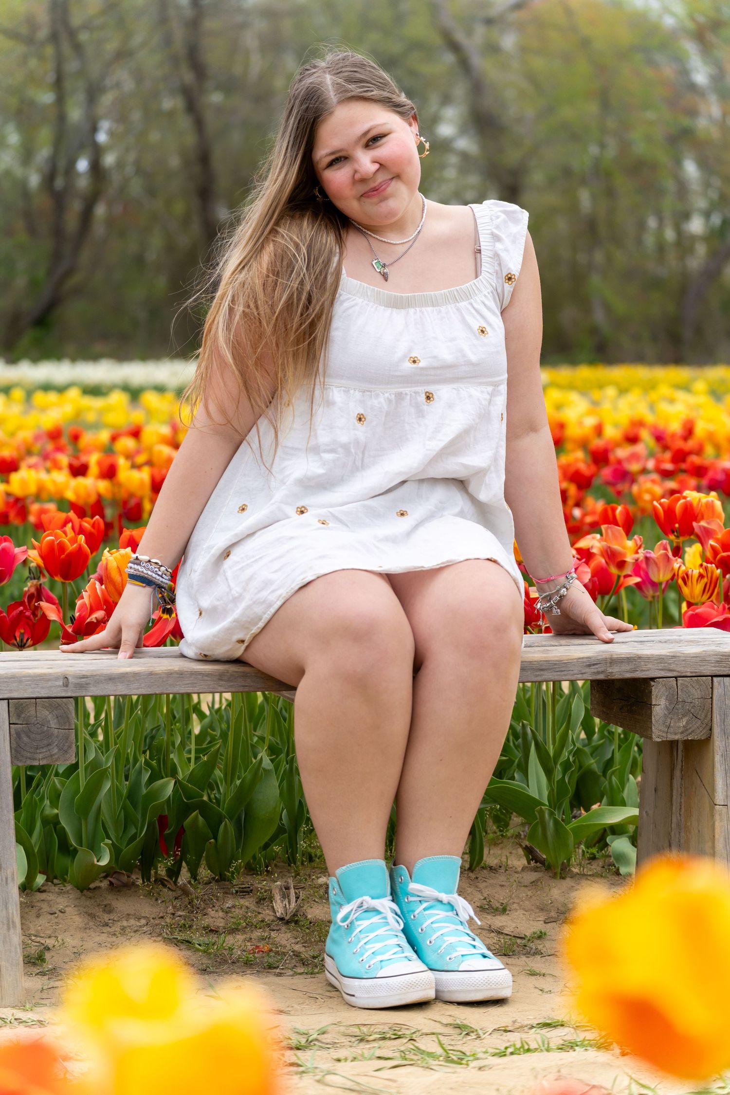 Someone in a white dress sits on a wooden bench surrounded by colorful tulips and daffodils.
