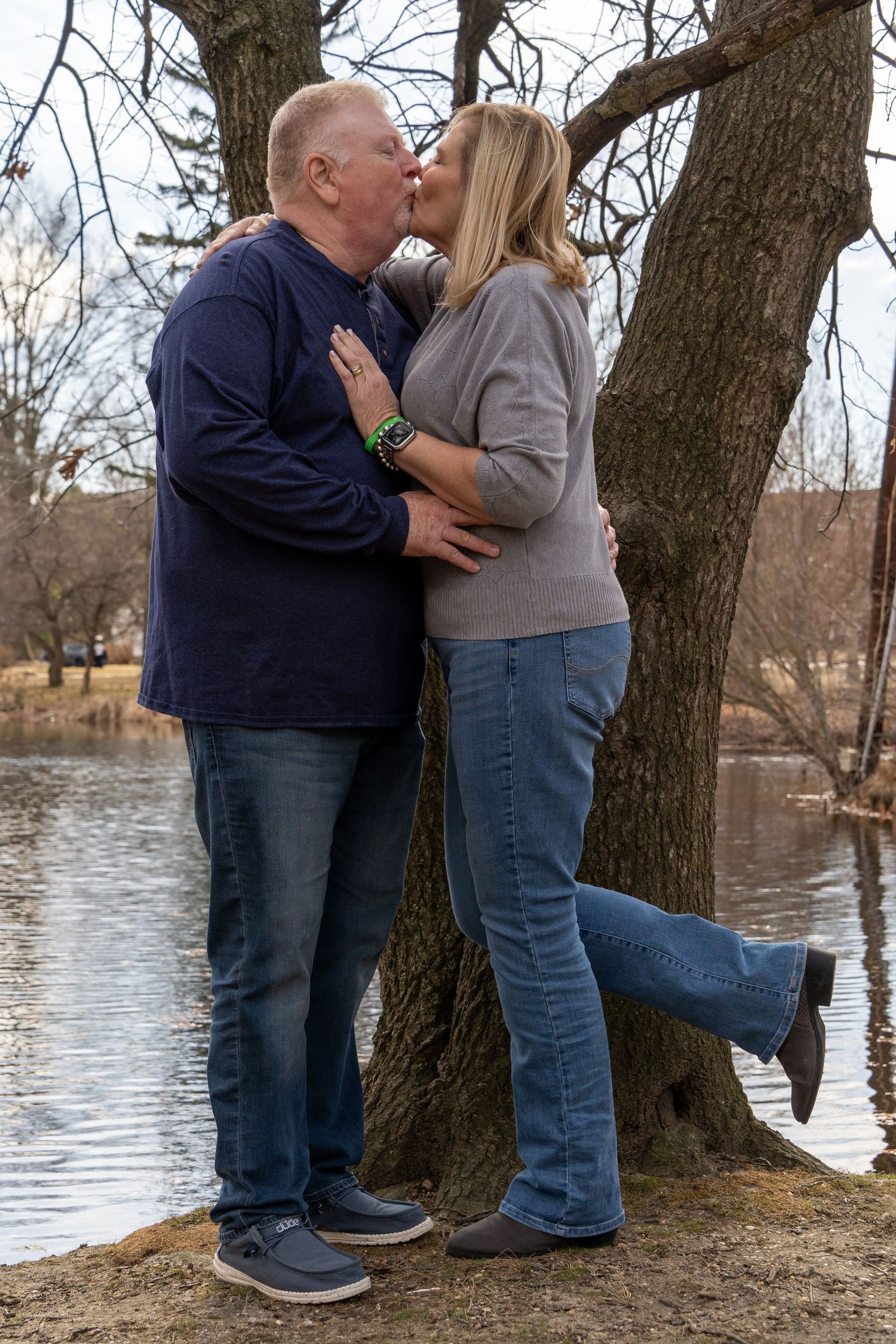 Romantic moment captured between couple by tree near water's edge.