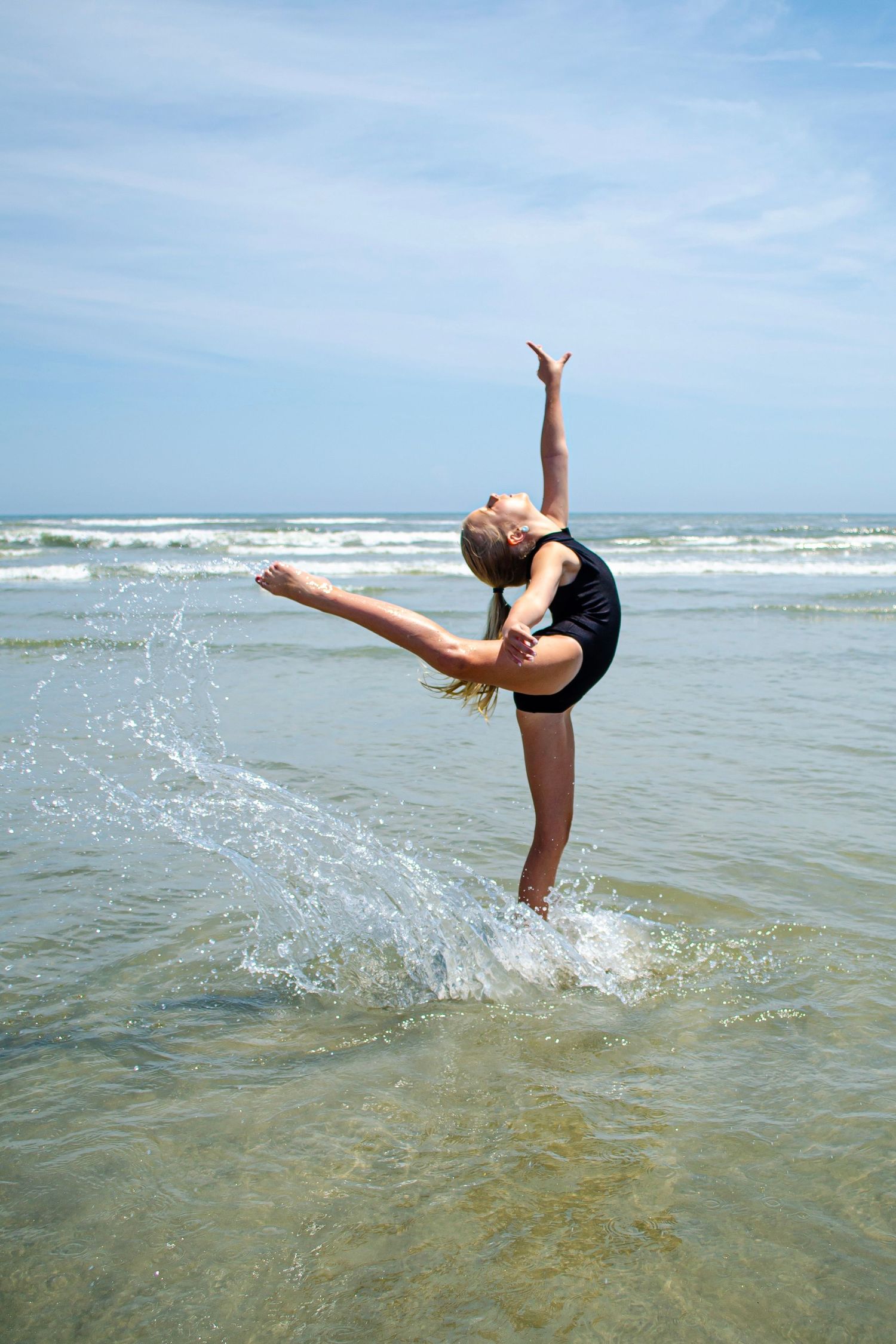 A graceful dance move executed in the ocean surf with water splashing dramatically.