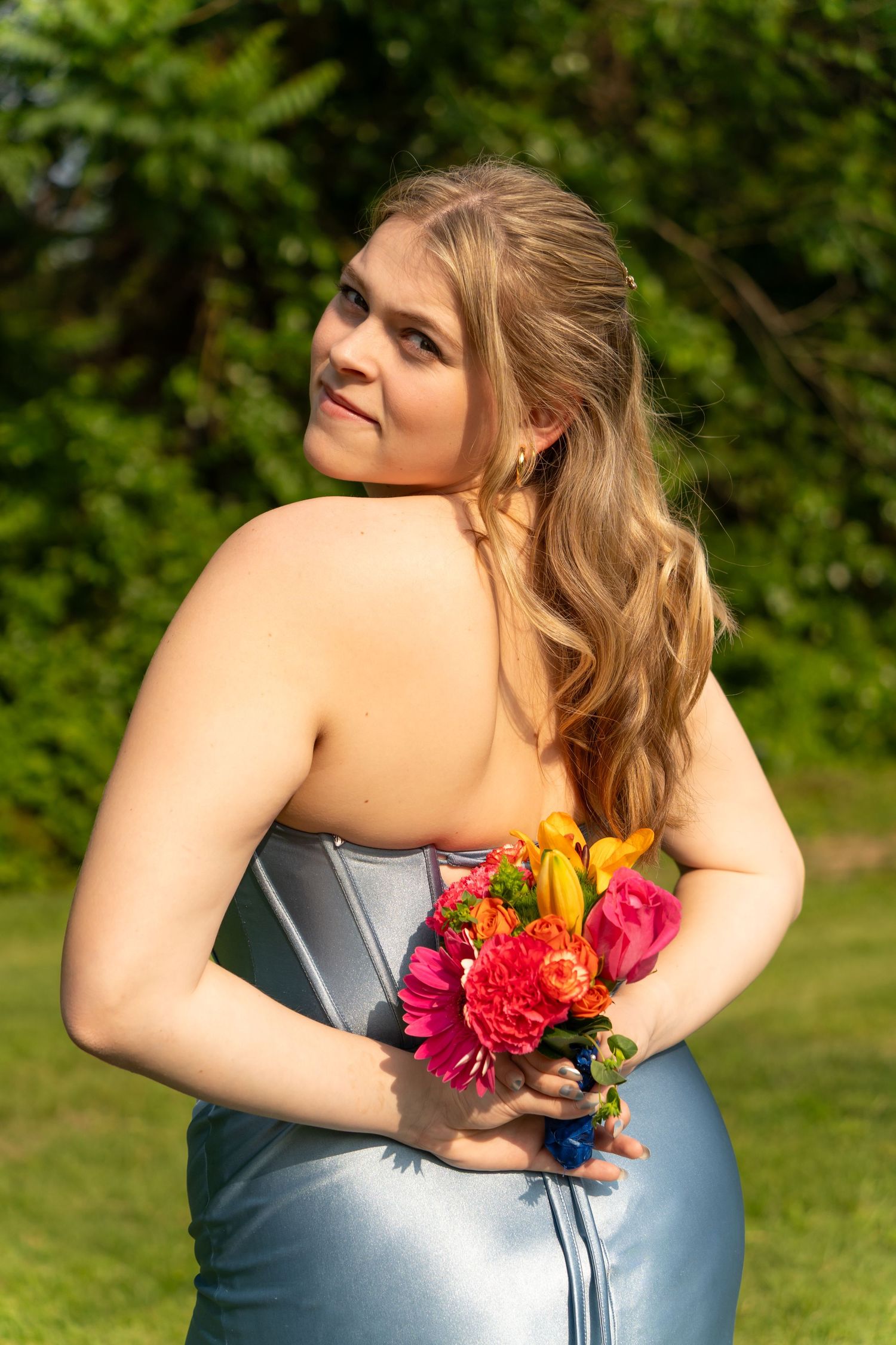 Elegant formal dress wearer holds vibrant bouquet against sunny garden background.