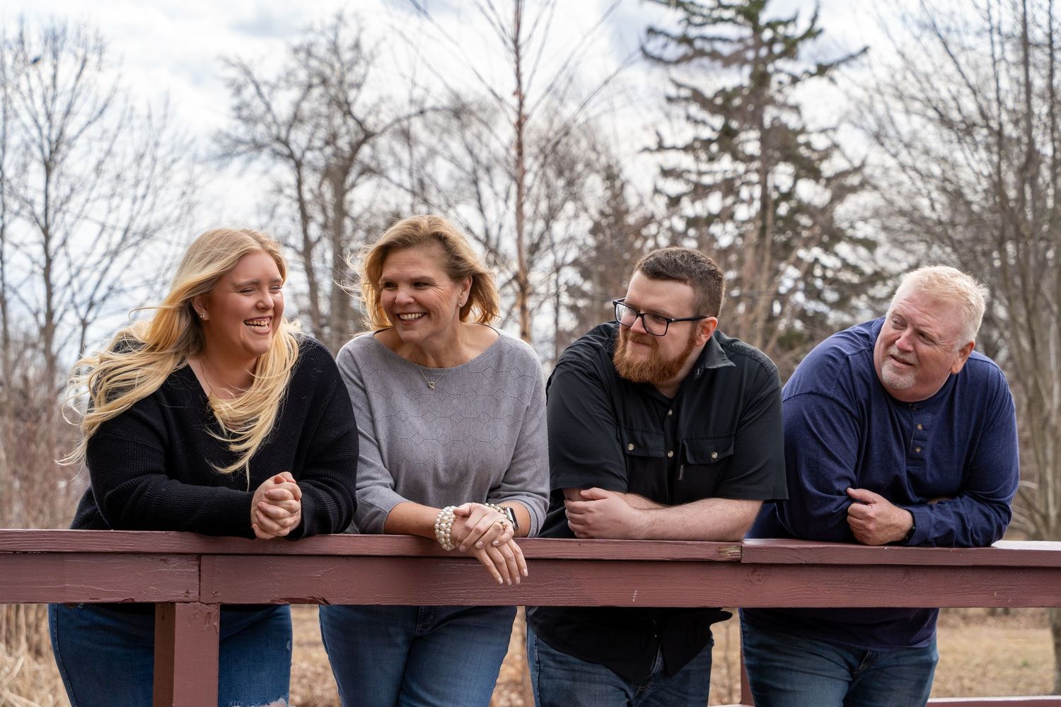 Family members gathered on a wooden bridge railing sharing laughs together.