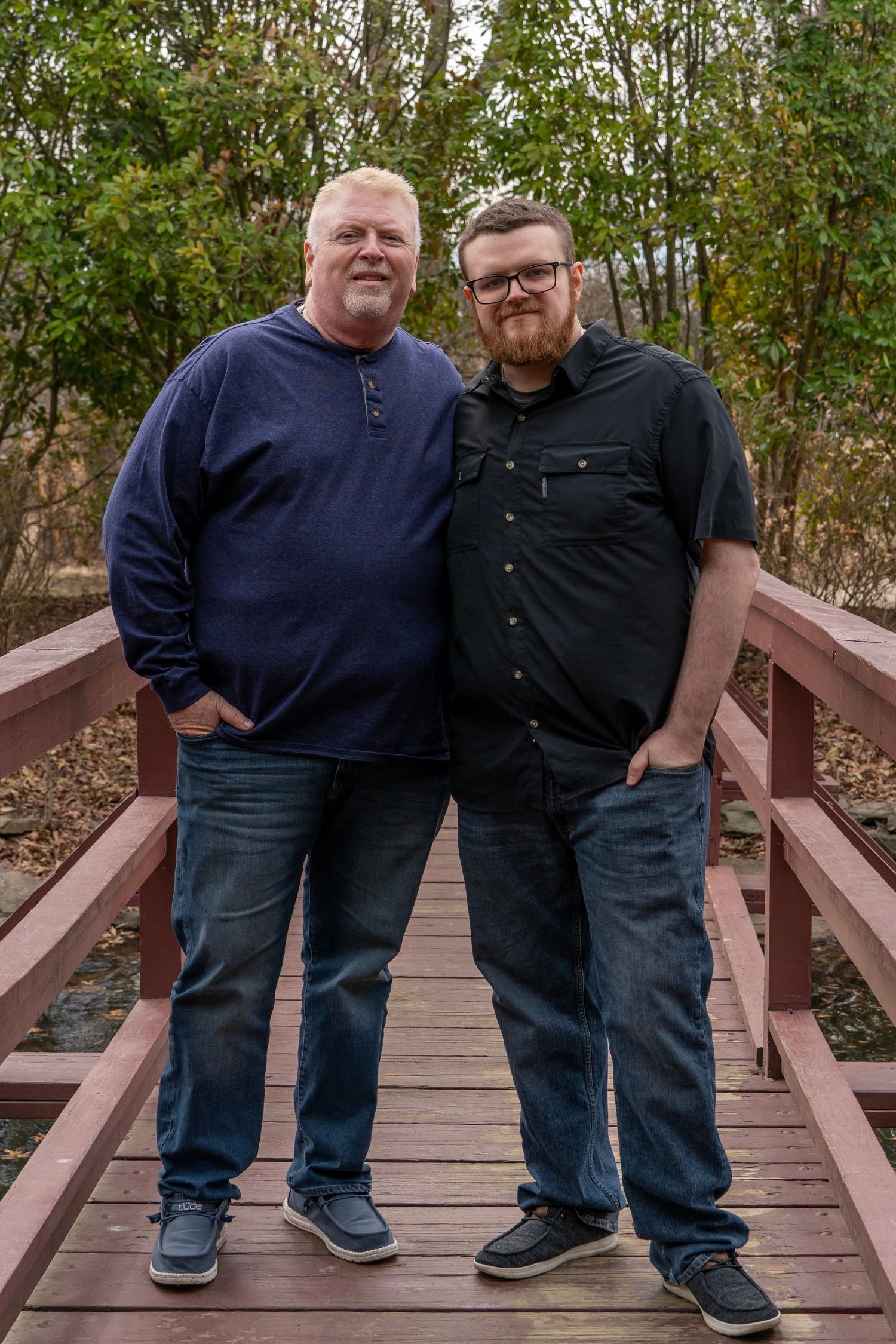 Father and son standing together on a wooden bridge deck in a casual outdoor setting.