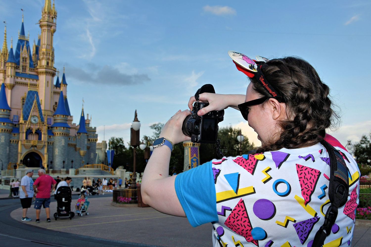 A panoramic view of Disney World castle with visitors taking photos in the foreground.