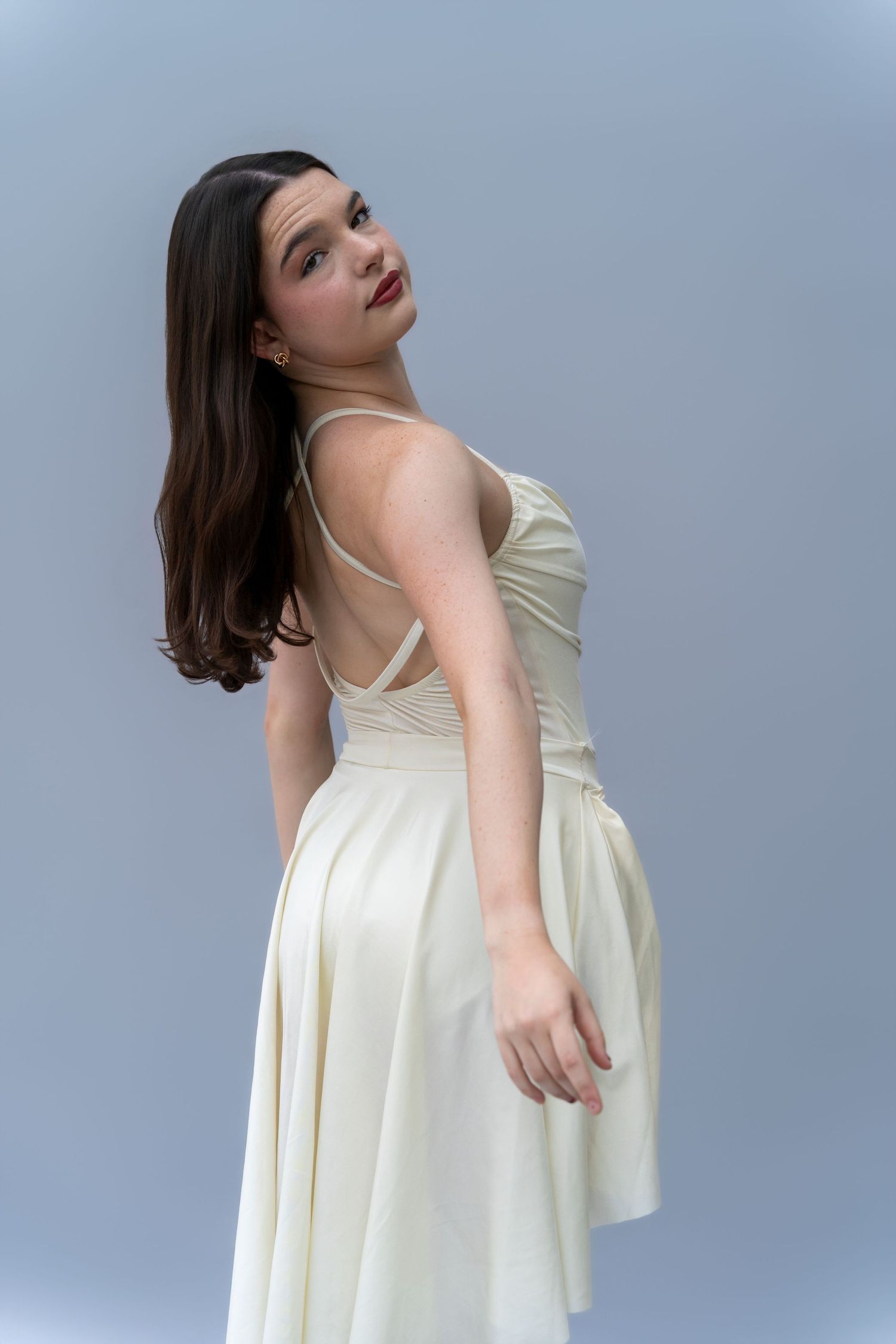 A person in a cream-colored sleeveless dress poses against a light blue background in a dynamic photo series.
