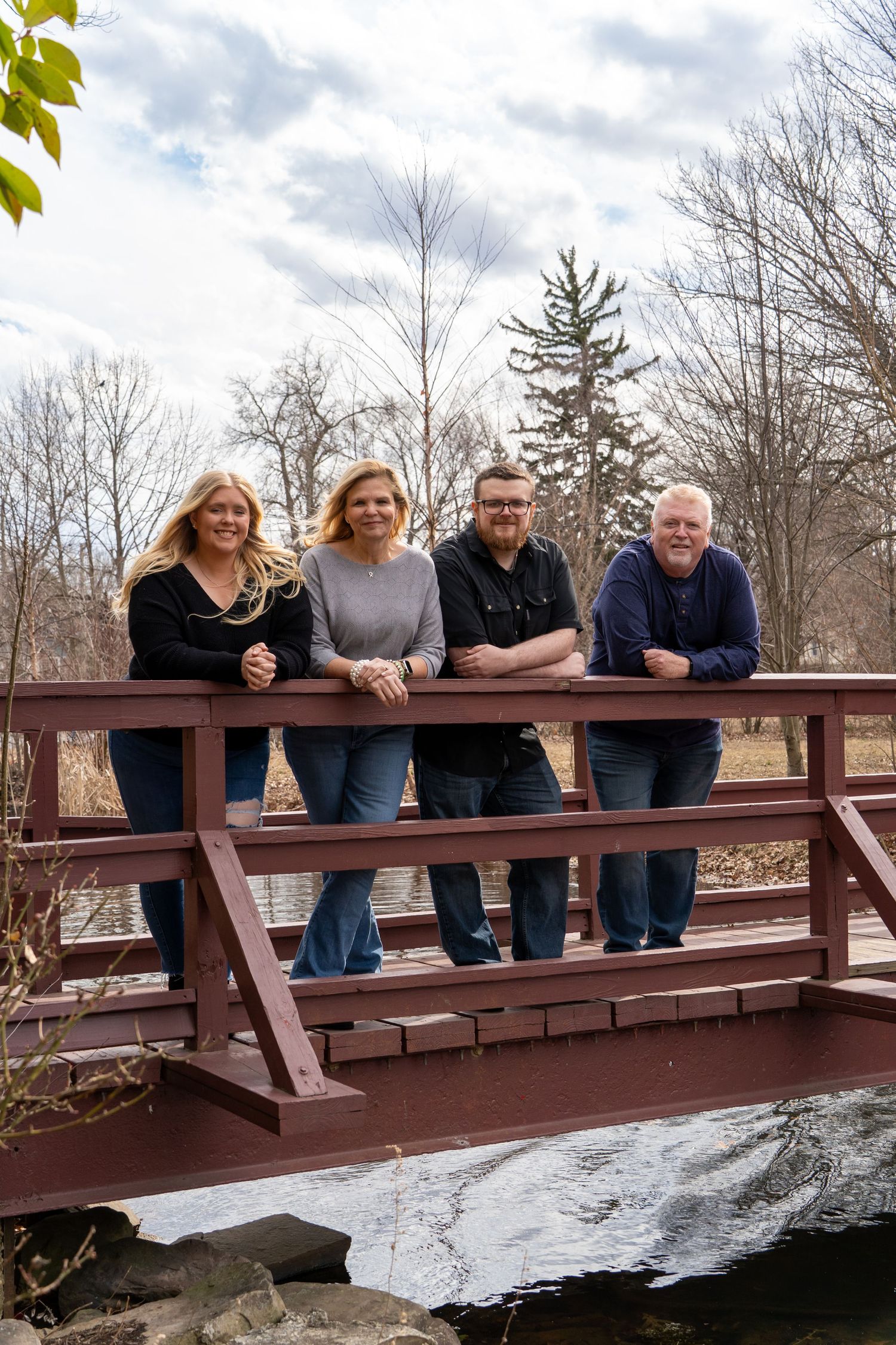 Family group posing together on wooden bridge over frozen stream in winter landscape.