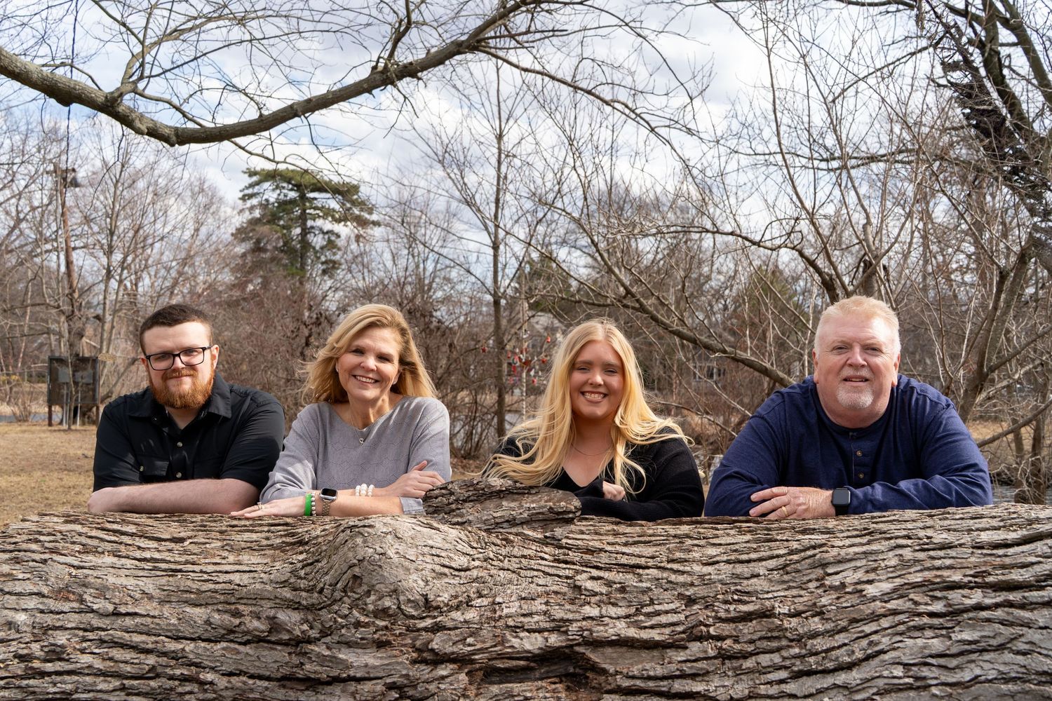 Family posing together while laying on a large fallen tree trunk in a park setting.