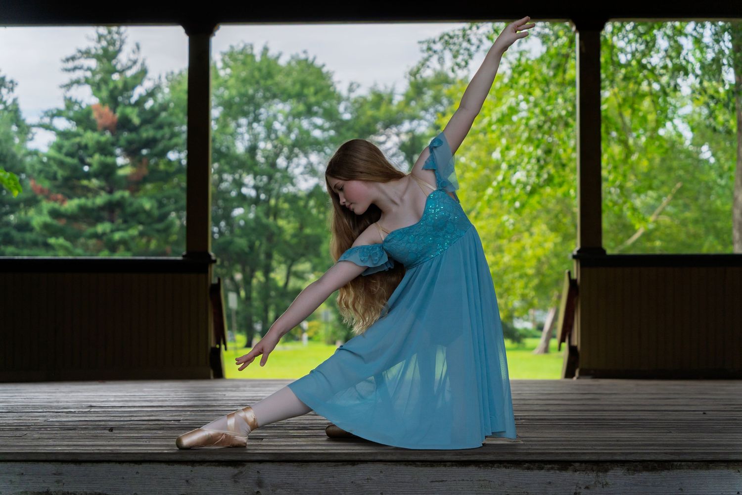 A dancer in a flowing turquoise dress strikes graceful poses on a rustic wooden porch surrounded by lush greenery.