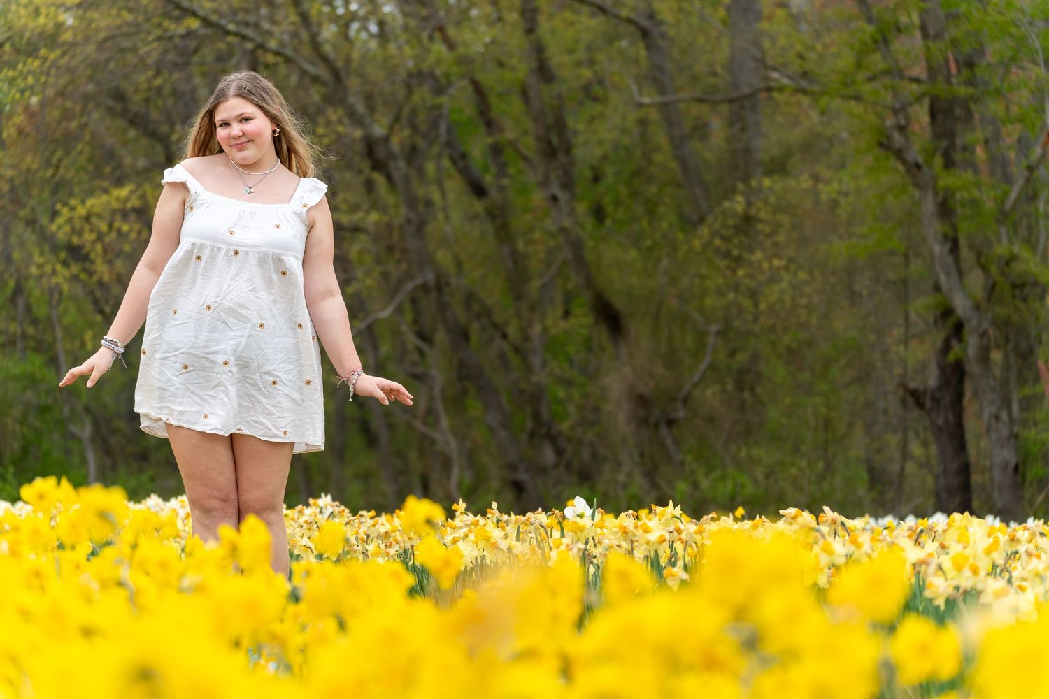 Woman twirling joyfully in a vibrant field of yellow wildflowers on a sunny spring day.