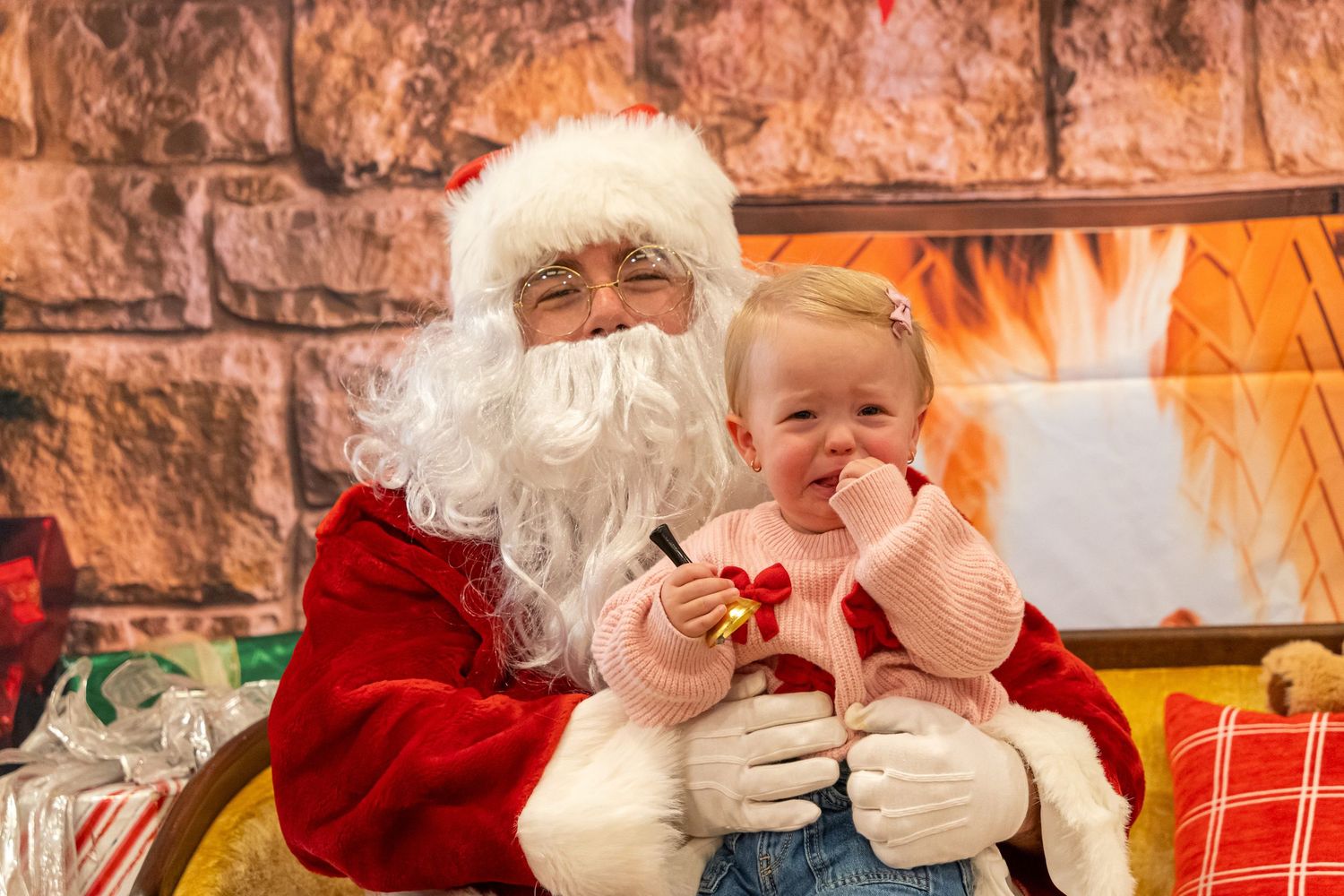 Holiday scene with Santa Claus and young child at festive indoor setting with fireplace.