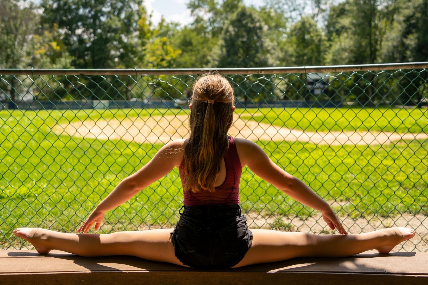 A dancer performs splits while sitting on an outdoor platform with a green field behind.