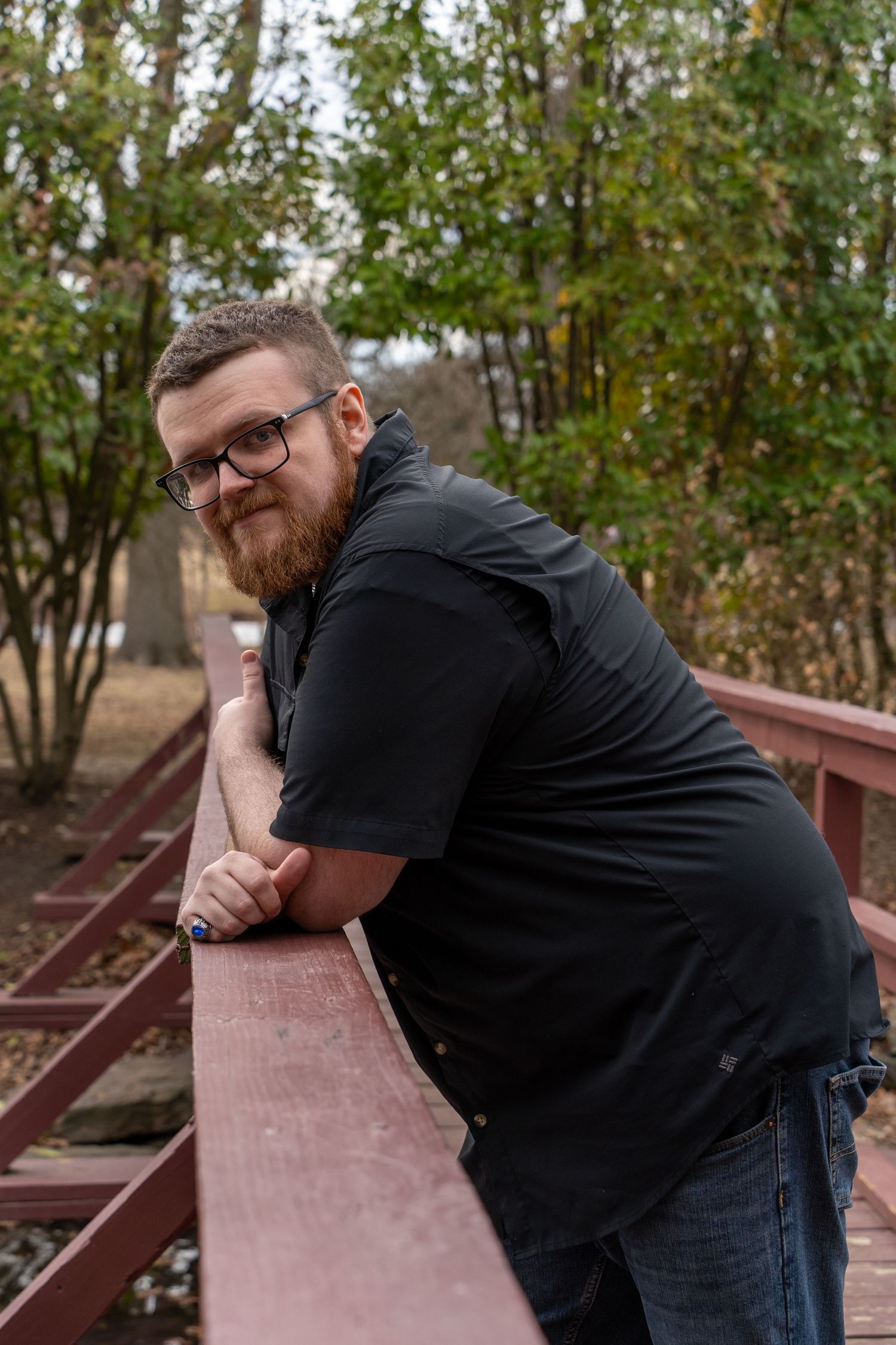Person in black shirt leaning on wooden railing outdoors.