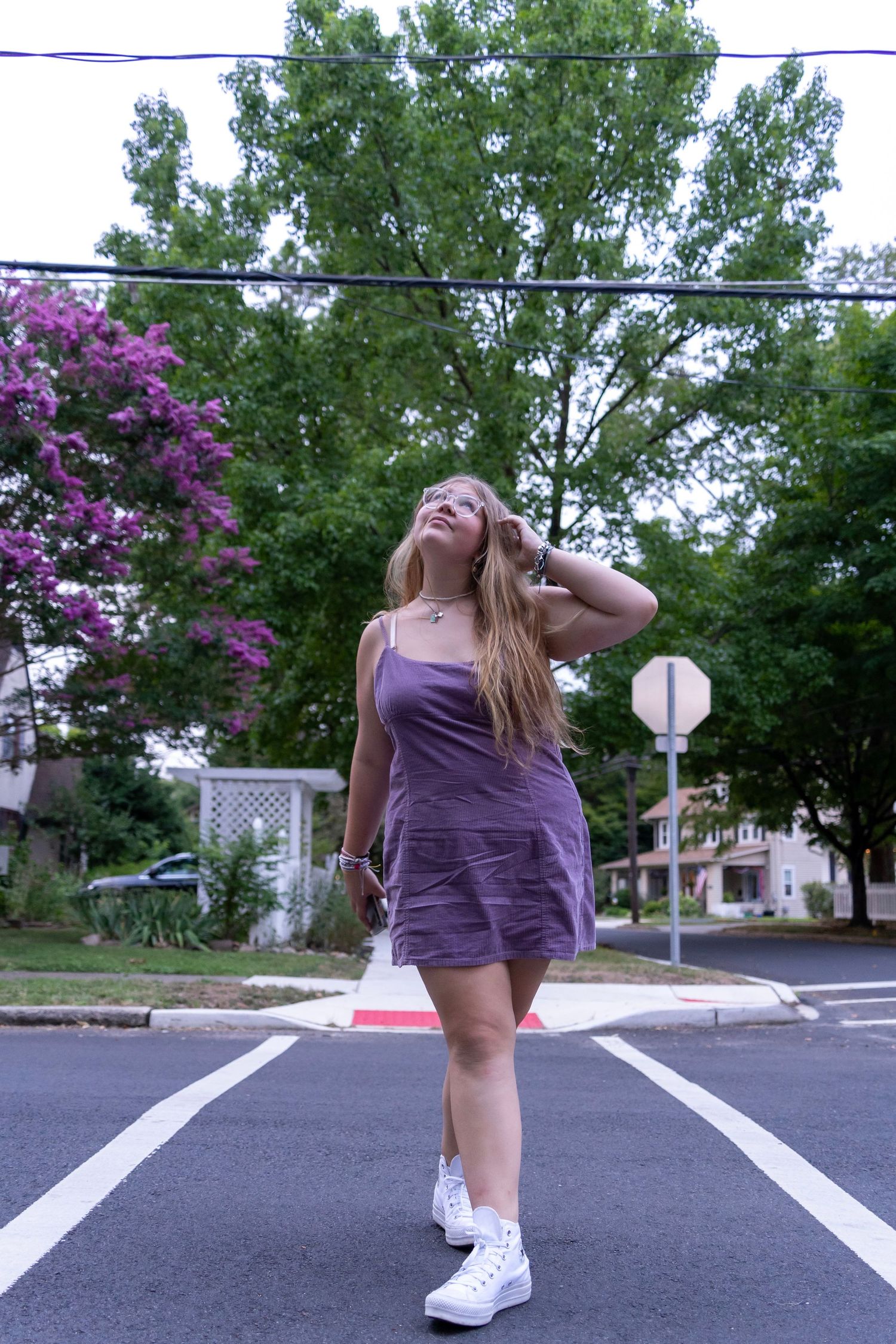 A dancer in purple performs playful poses on an asphalt street.
