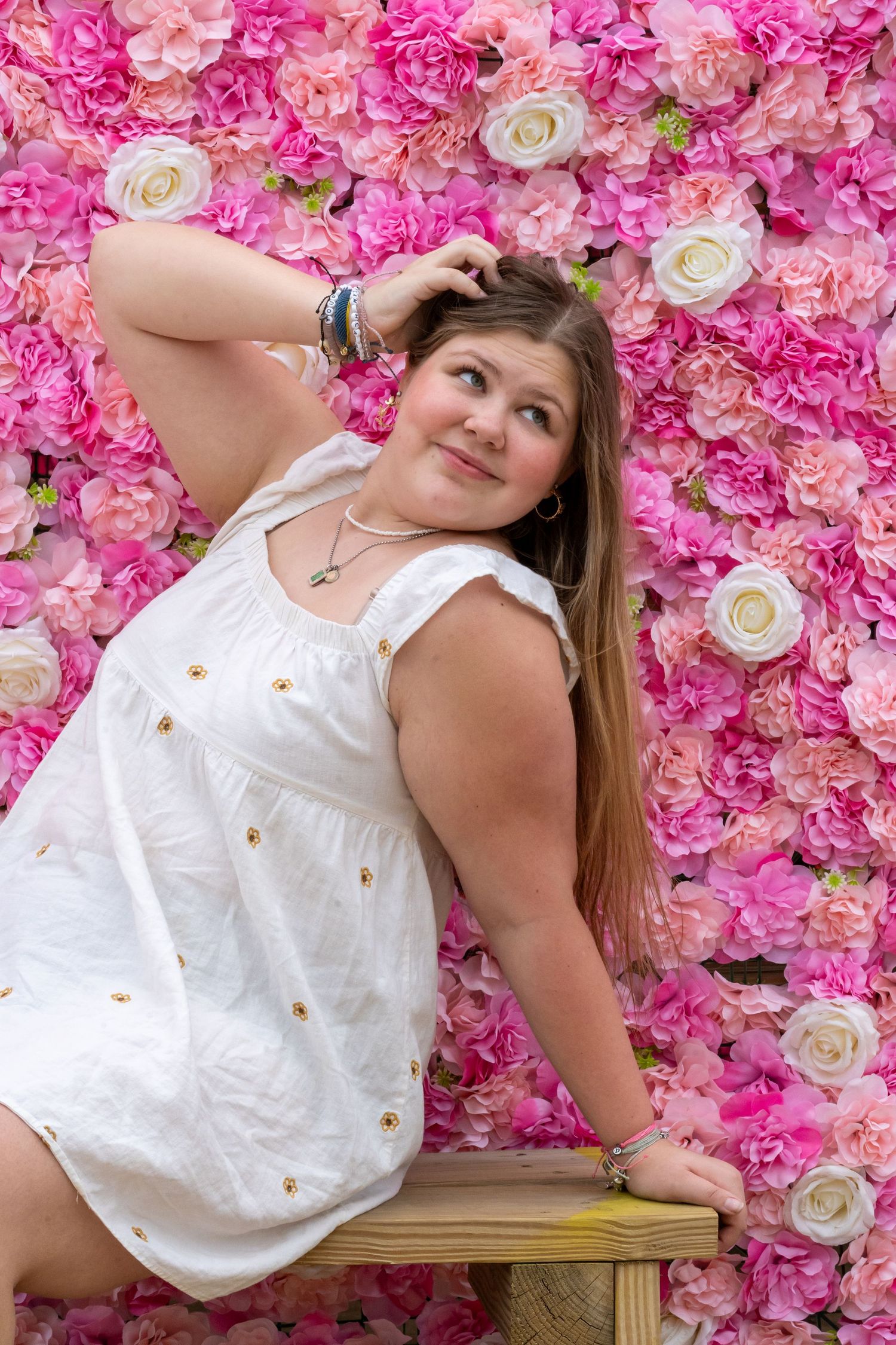 A white floral dress photographed against a backdrop of pink roses and flowers.