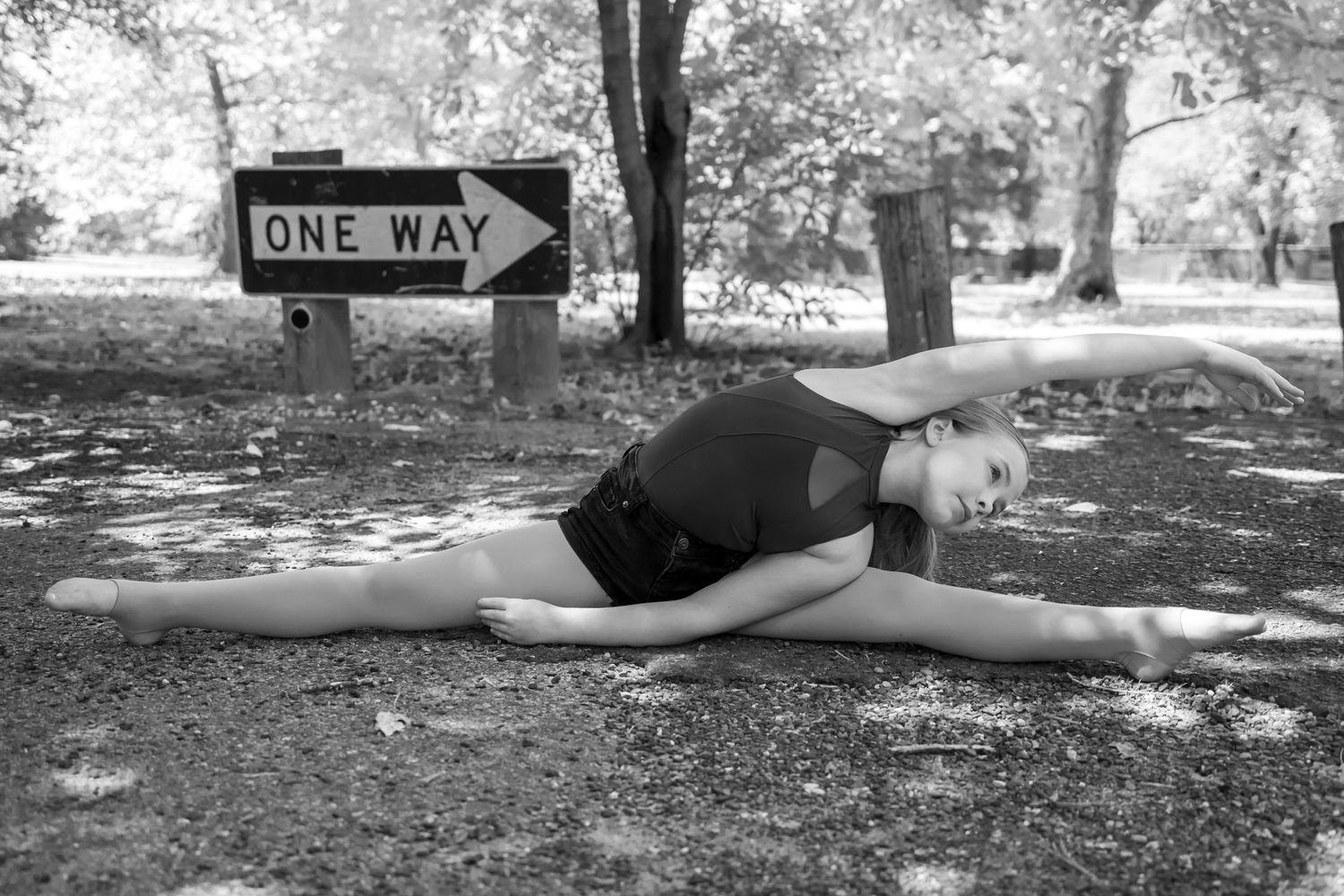 A black and white photo of someone stretching on grass near a one way sign.