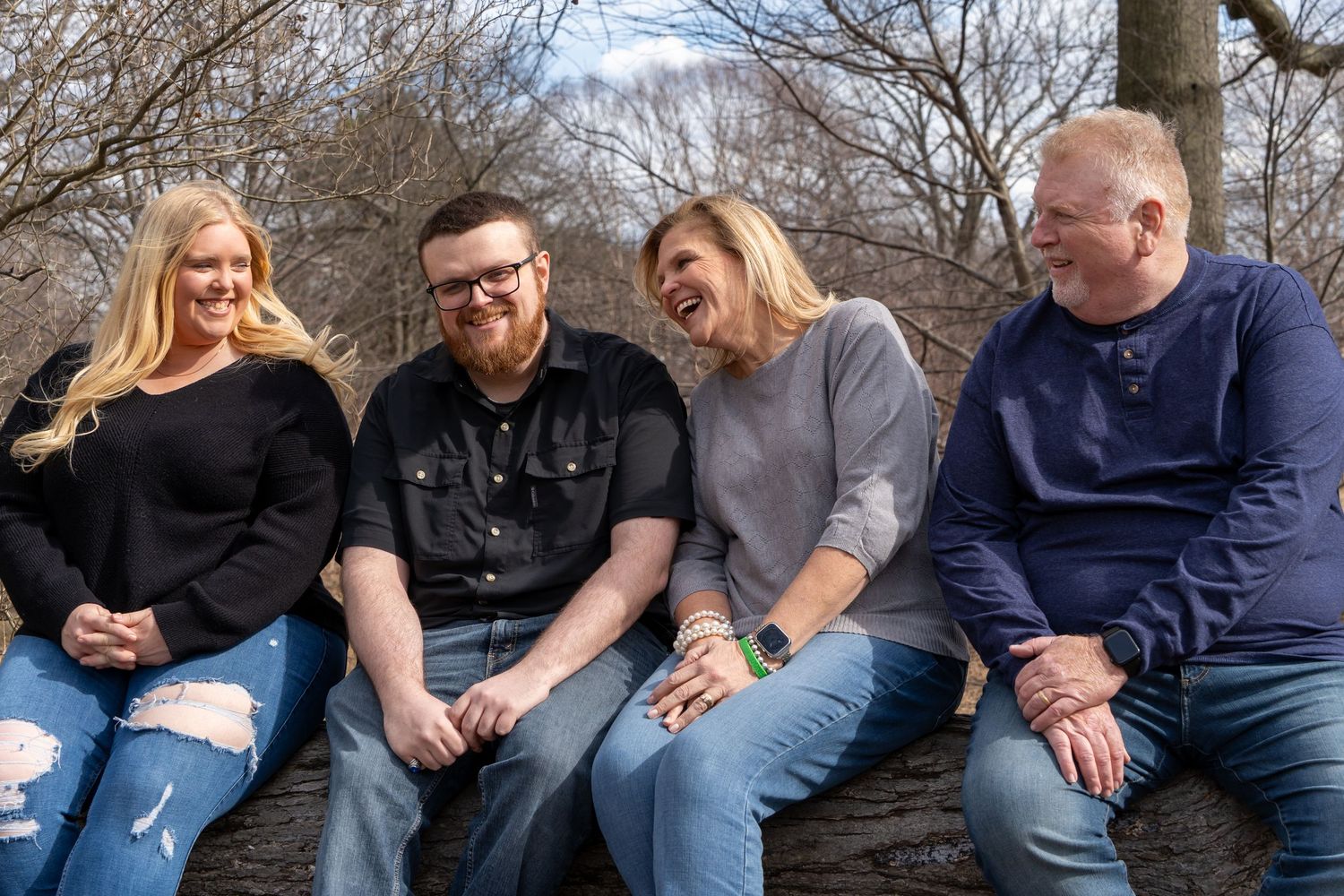 Family sitting casually together on wooden log during outdoor portrait session.