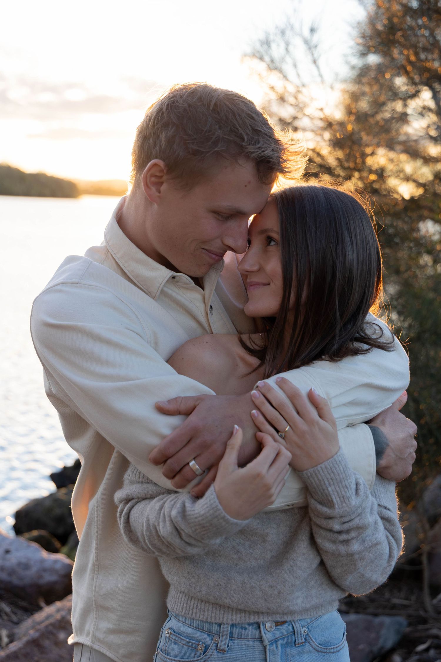 A couple cuddling each other at sunset at a lake.