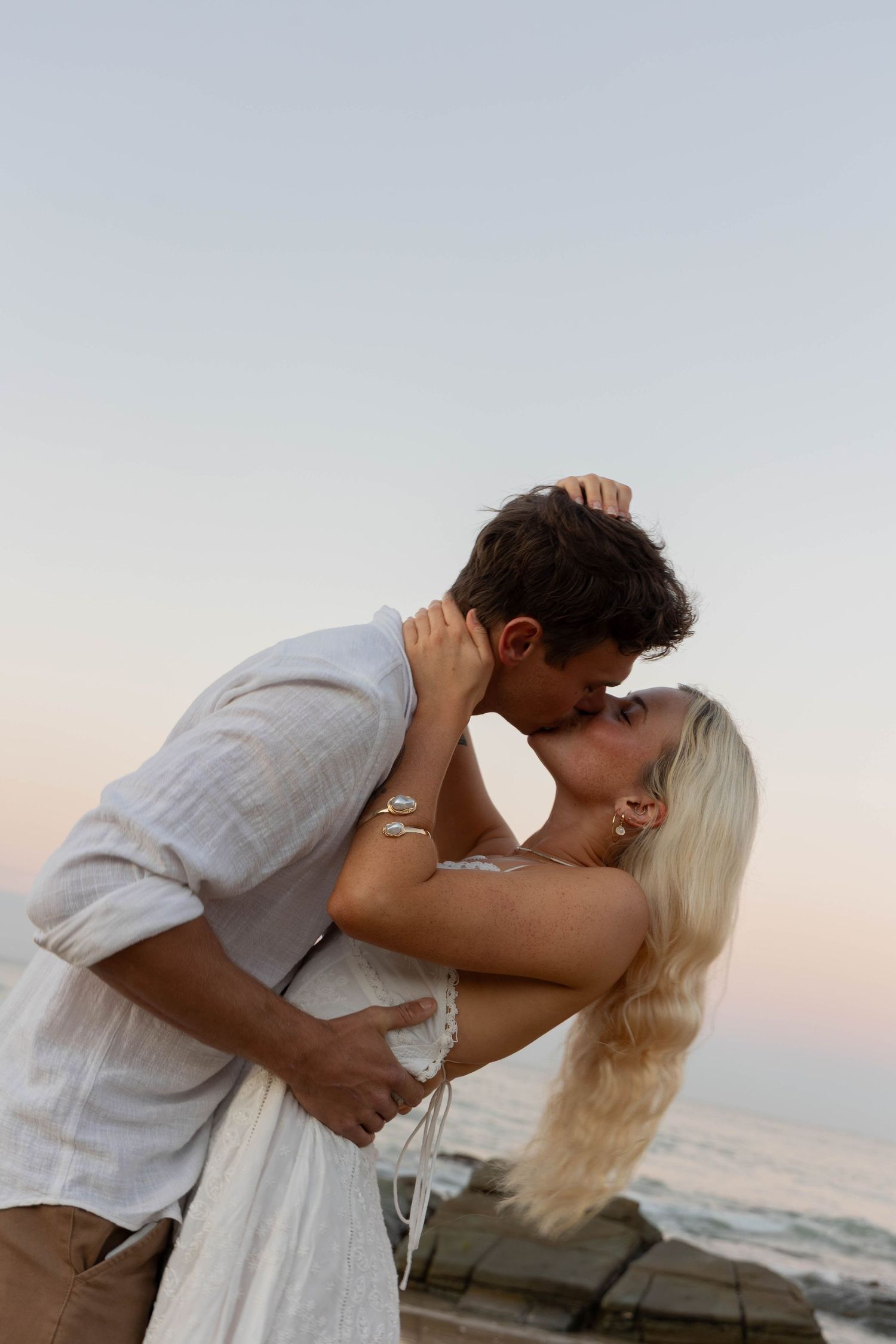 A couple kissing in front of a camera at sunset.