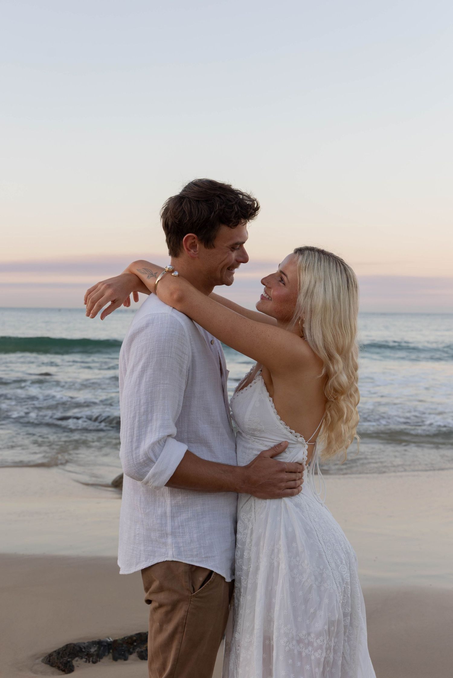 Shows a couple posing for their couple photos at sunset on the beach.