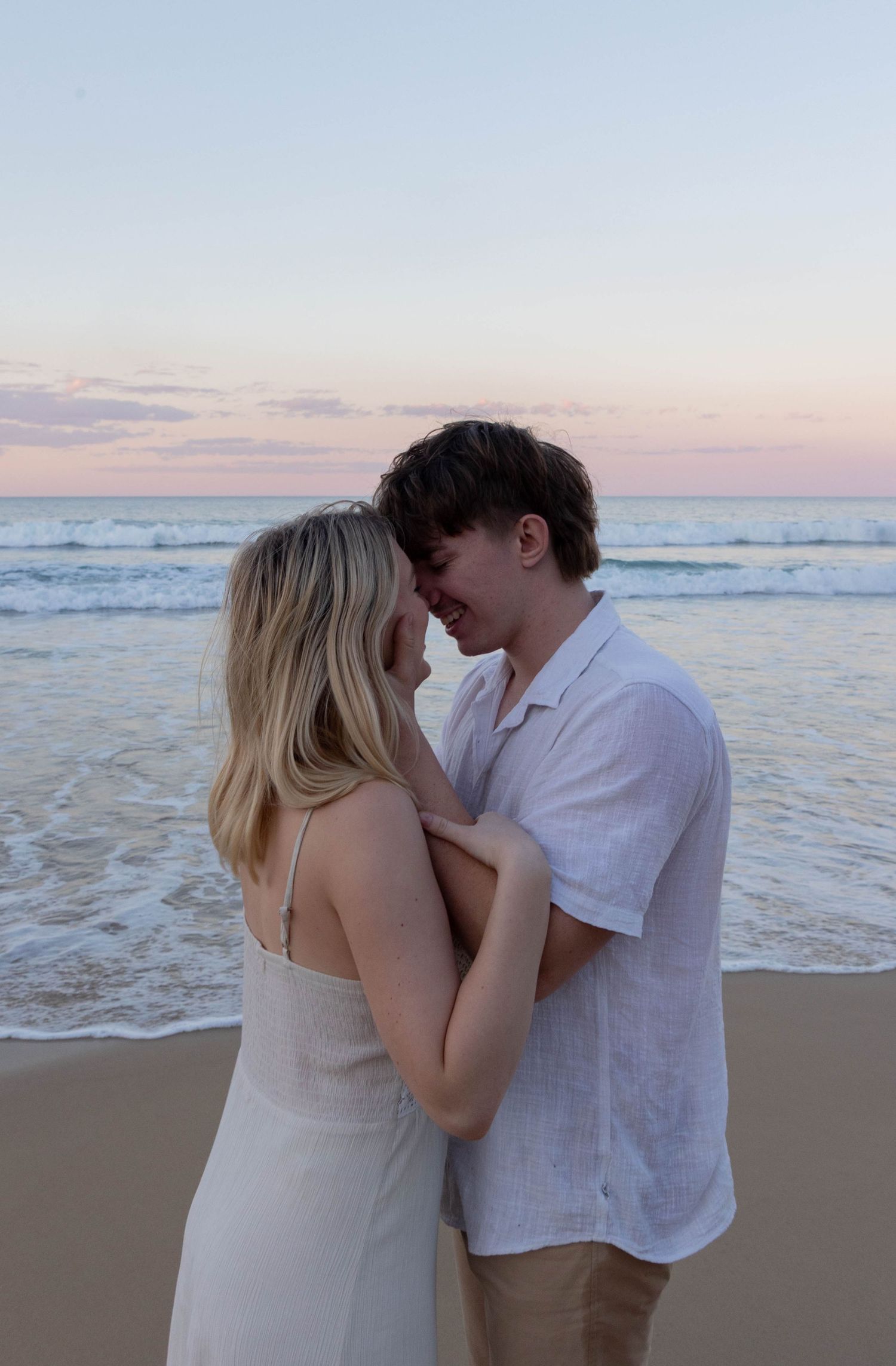 Shows a couple cuddling on the beach at sunset.