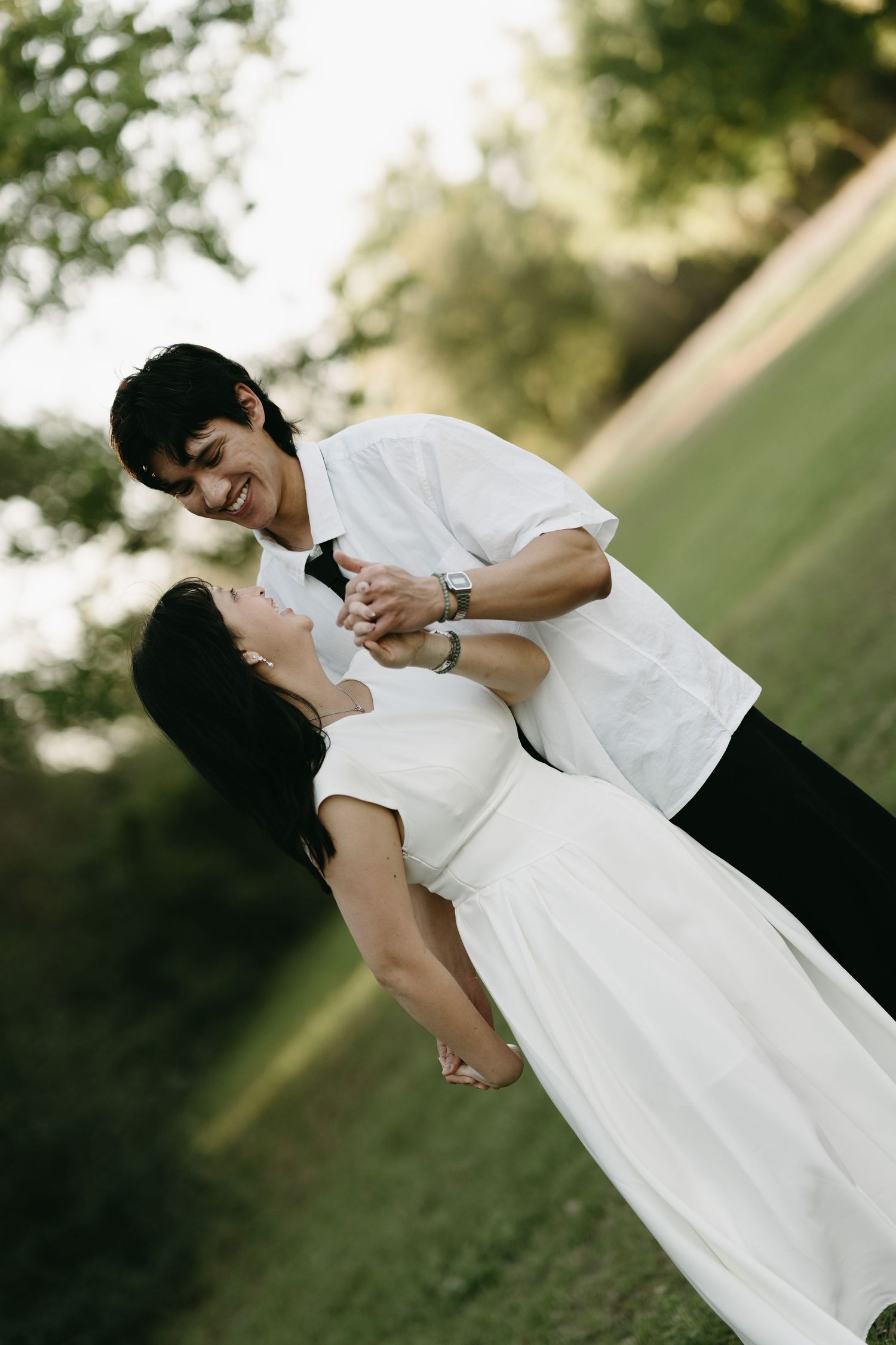 A romantic couple in white outfits share a tender moment while dancing together in a sunlit outdoor setting.