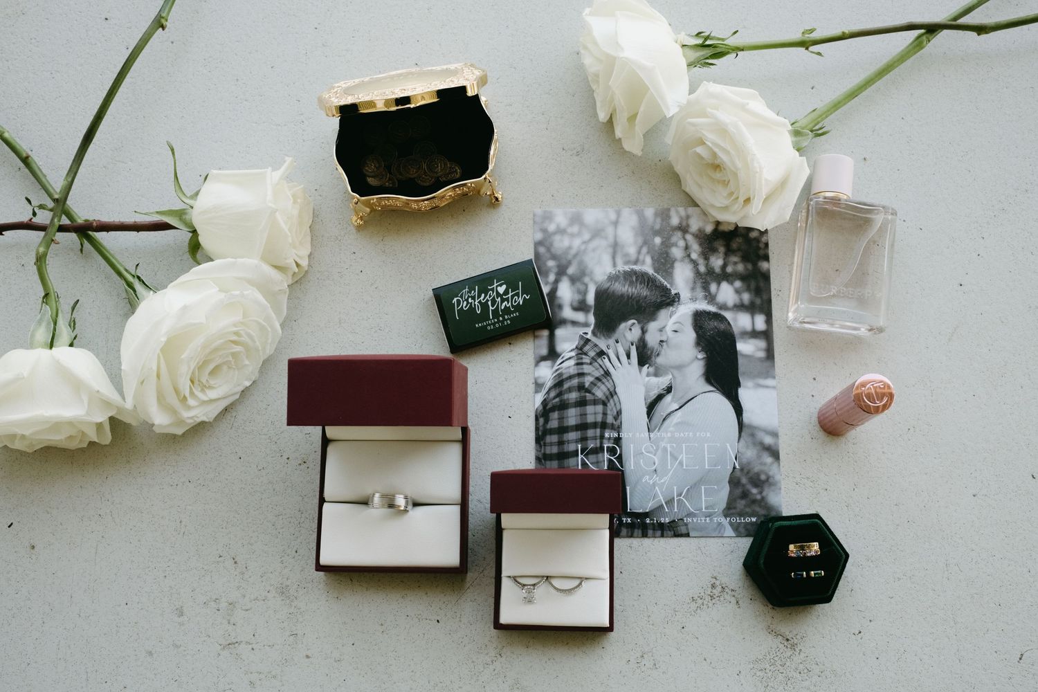 Flatlay photography of white roses, jewelry boxes, and wedding accessories arranged on a light gray surface.