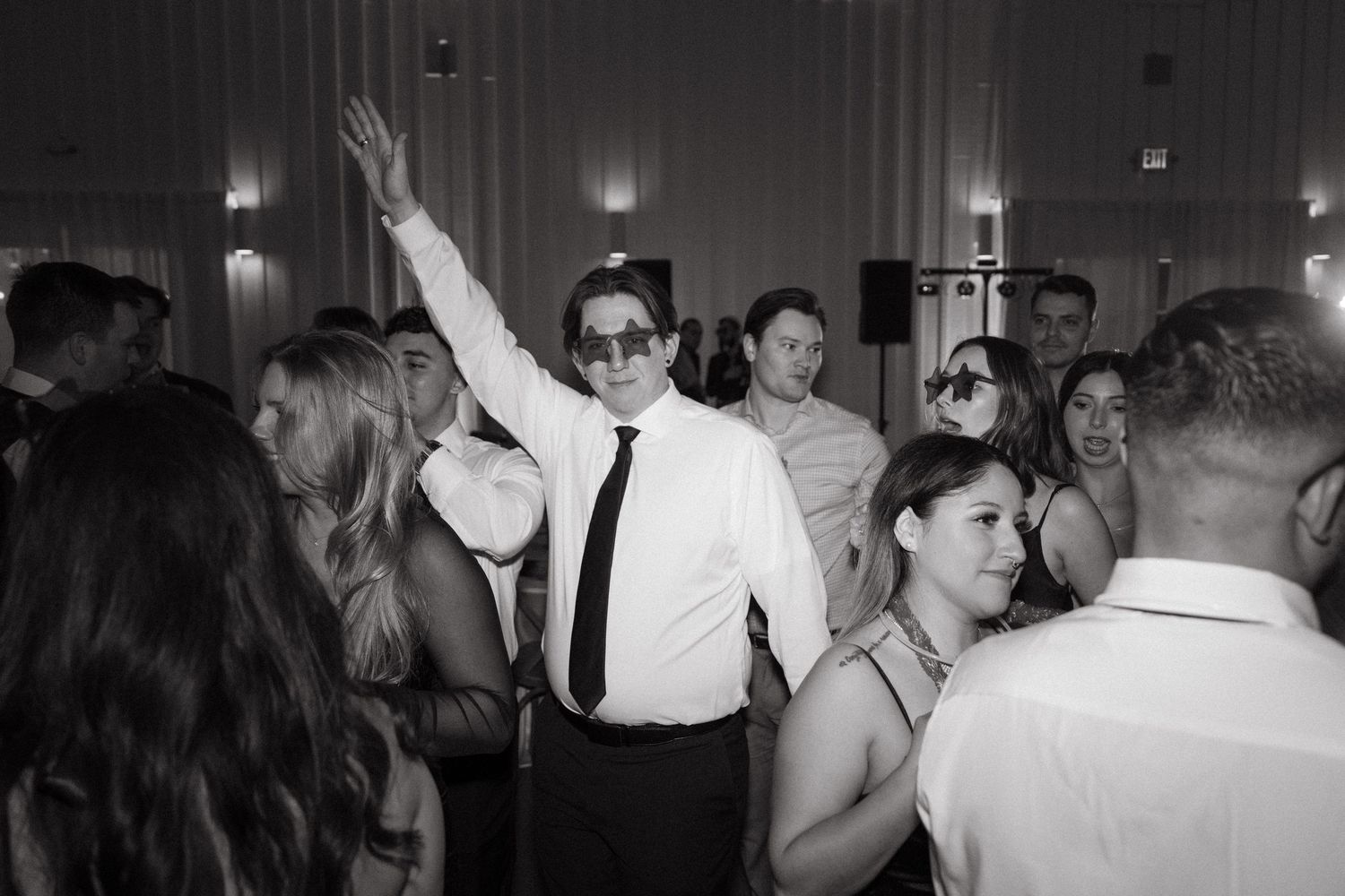 Black and white photo of a crowded dance floor at a wedding reception with guests dancing under dim lighting.