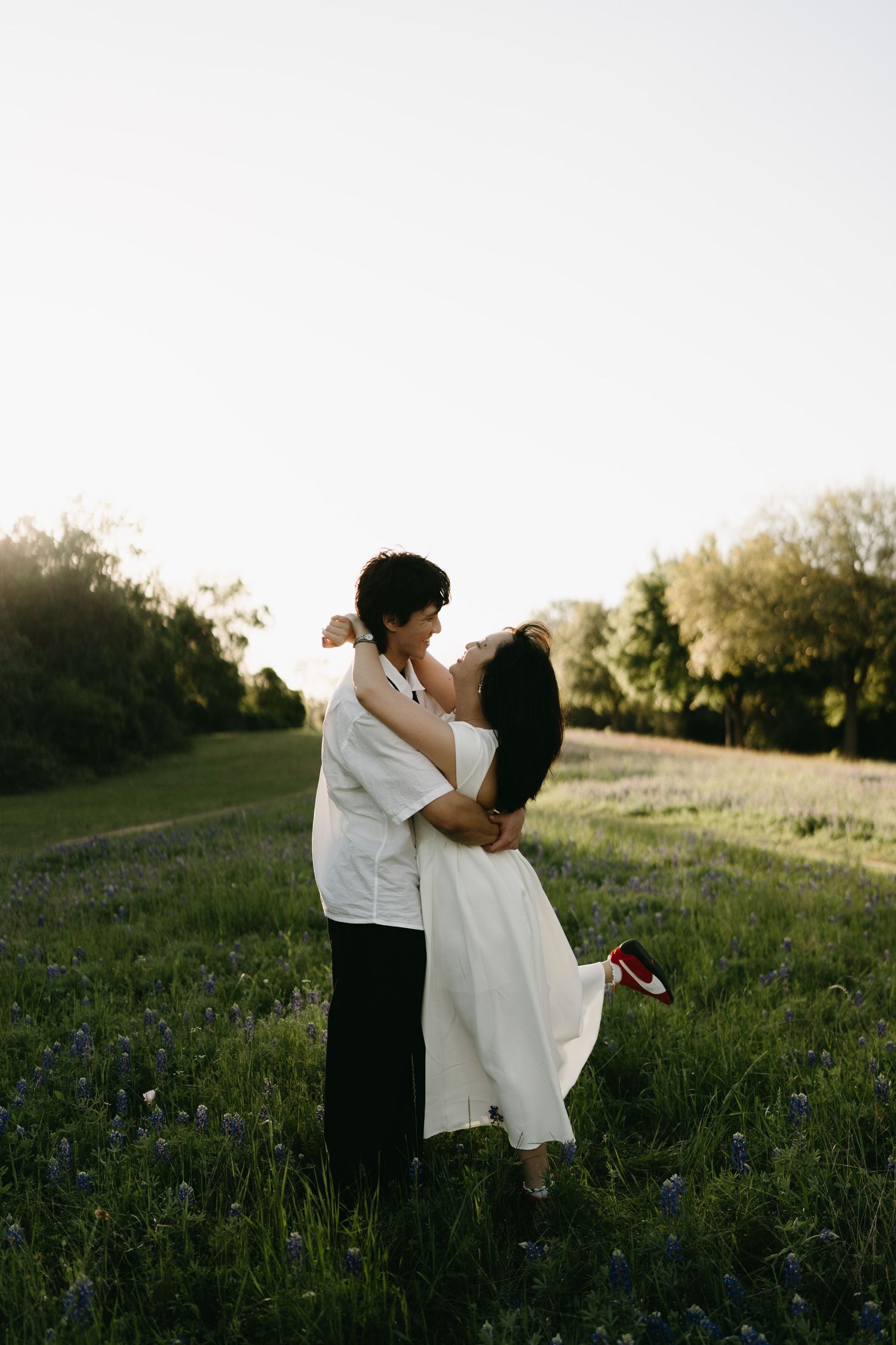 A couple embraces in a sunlit meadow filled with wildflowers during golden hour.