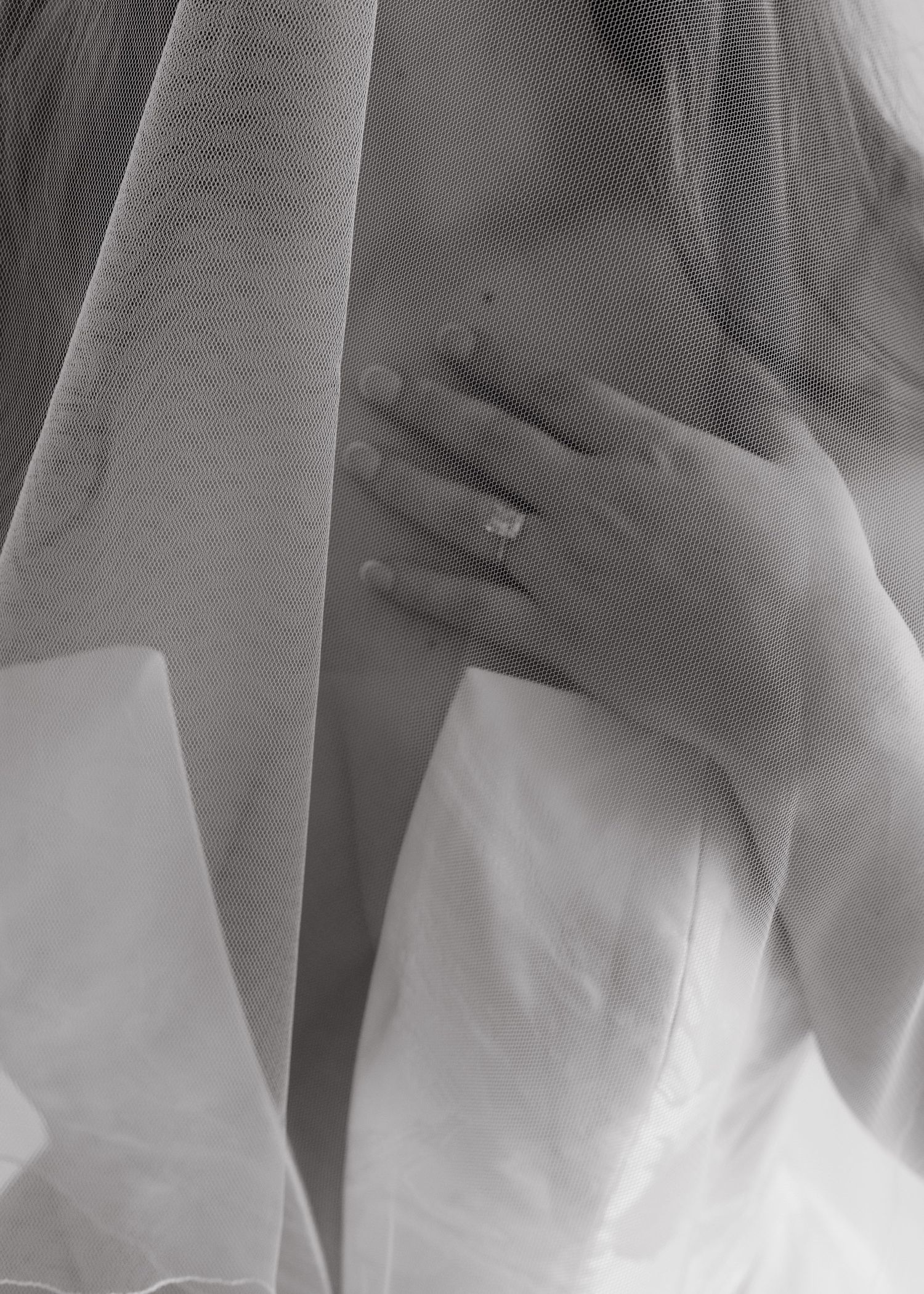 Black and white photo of a bride holding her robe closed, showcasing a diamond engagement ring on her finger.