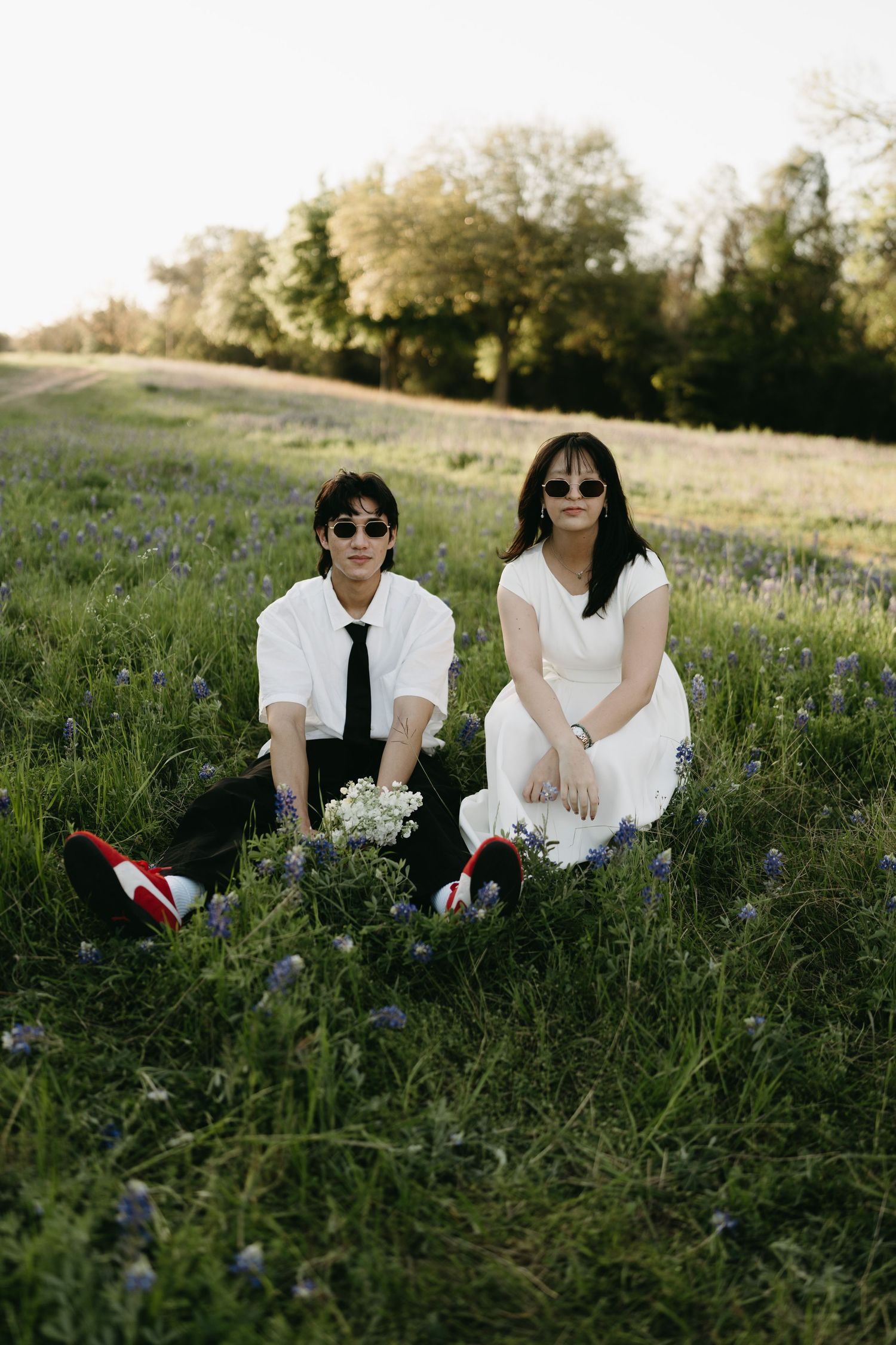 Two people in white outfits sit together in a blooming wildflower field during golden hour.