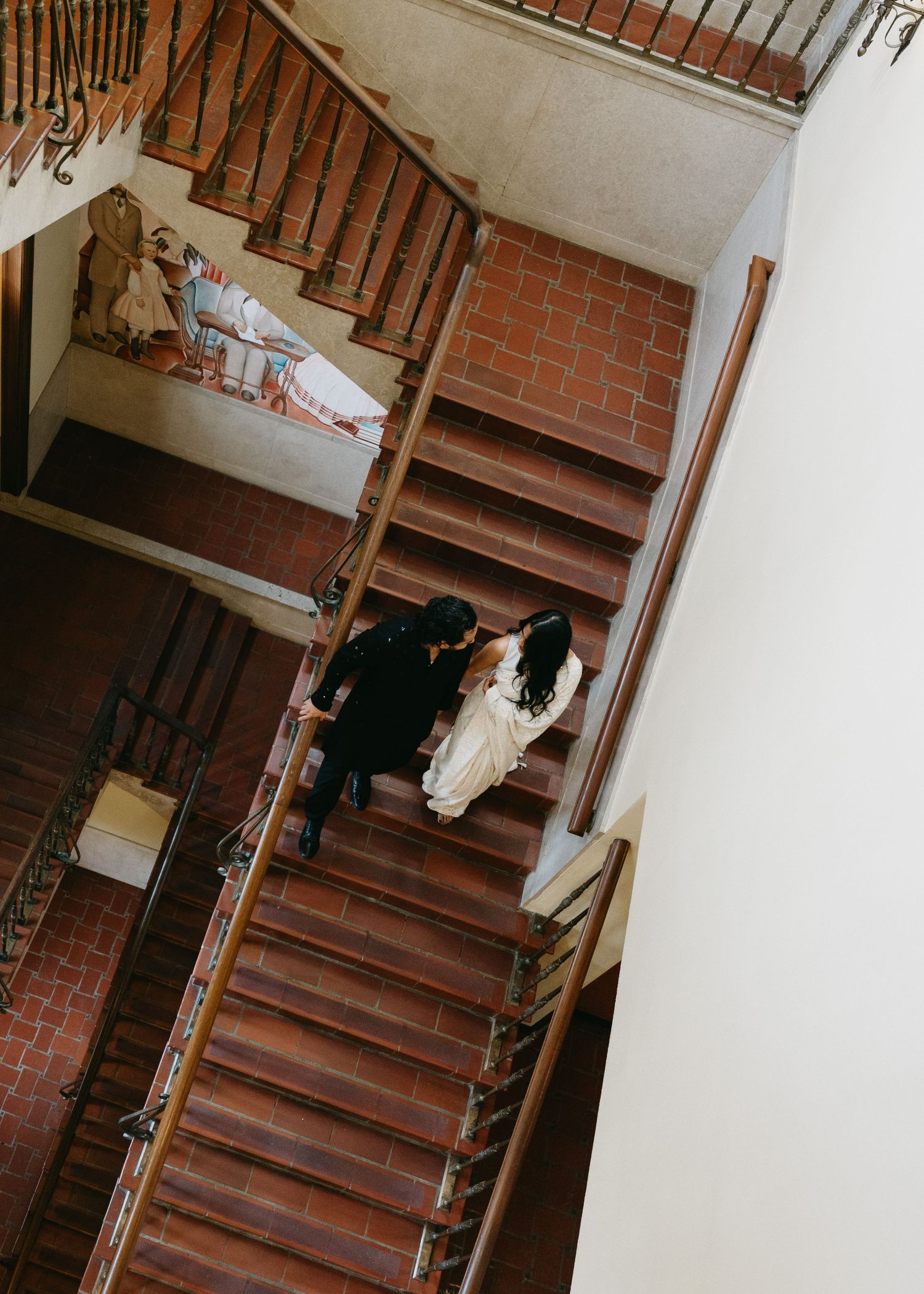 Aerial view of a bride and groom walking down terracotta brick stairs in an elegant venue.