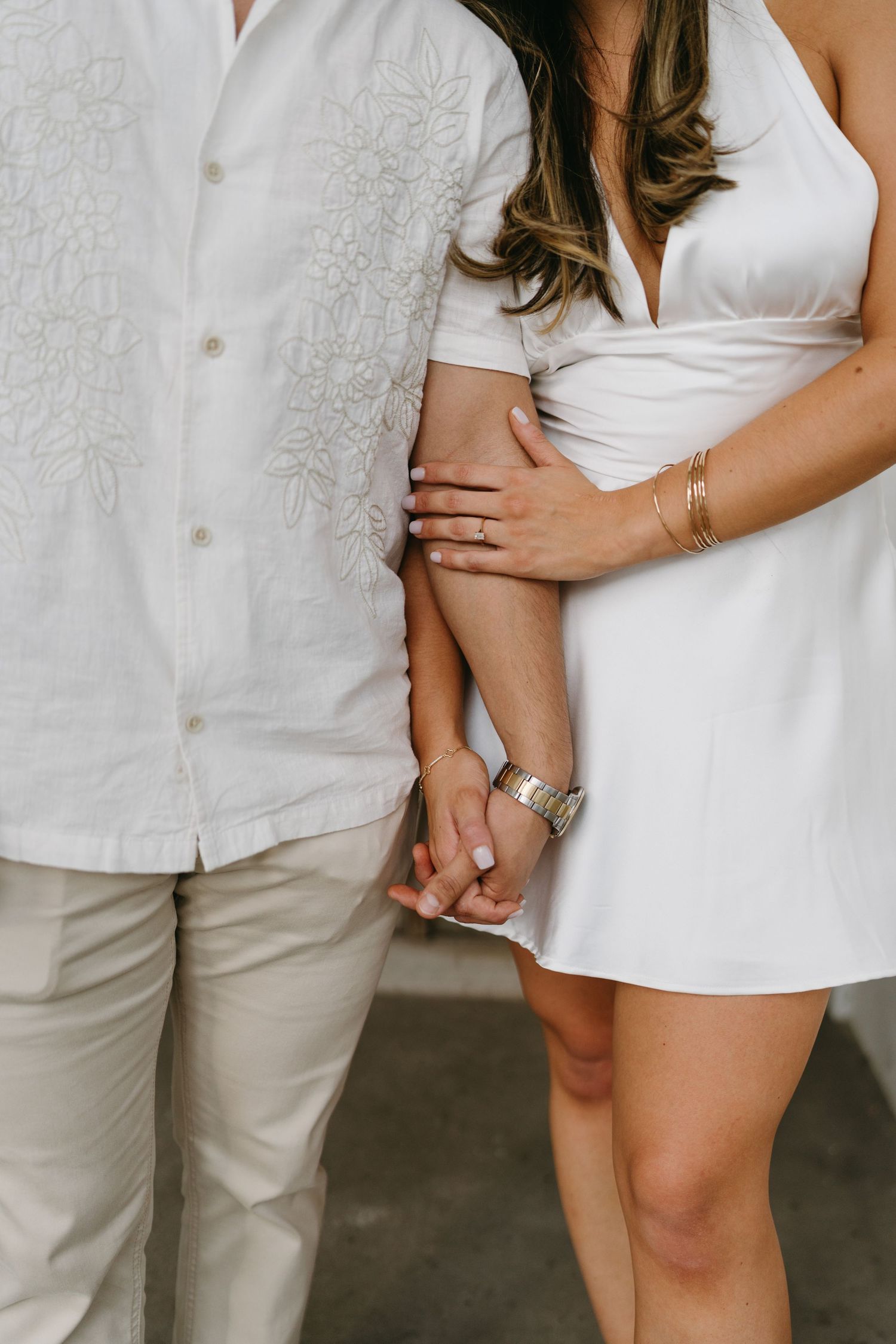 Couple in coordinated white and beige outfits embracing in a romantic outdoor photoshoot.