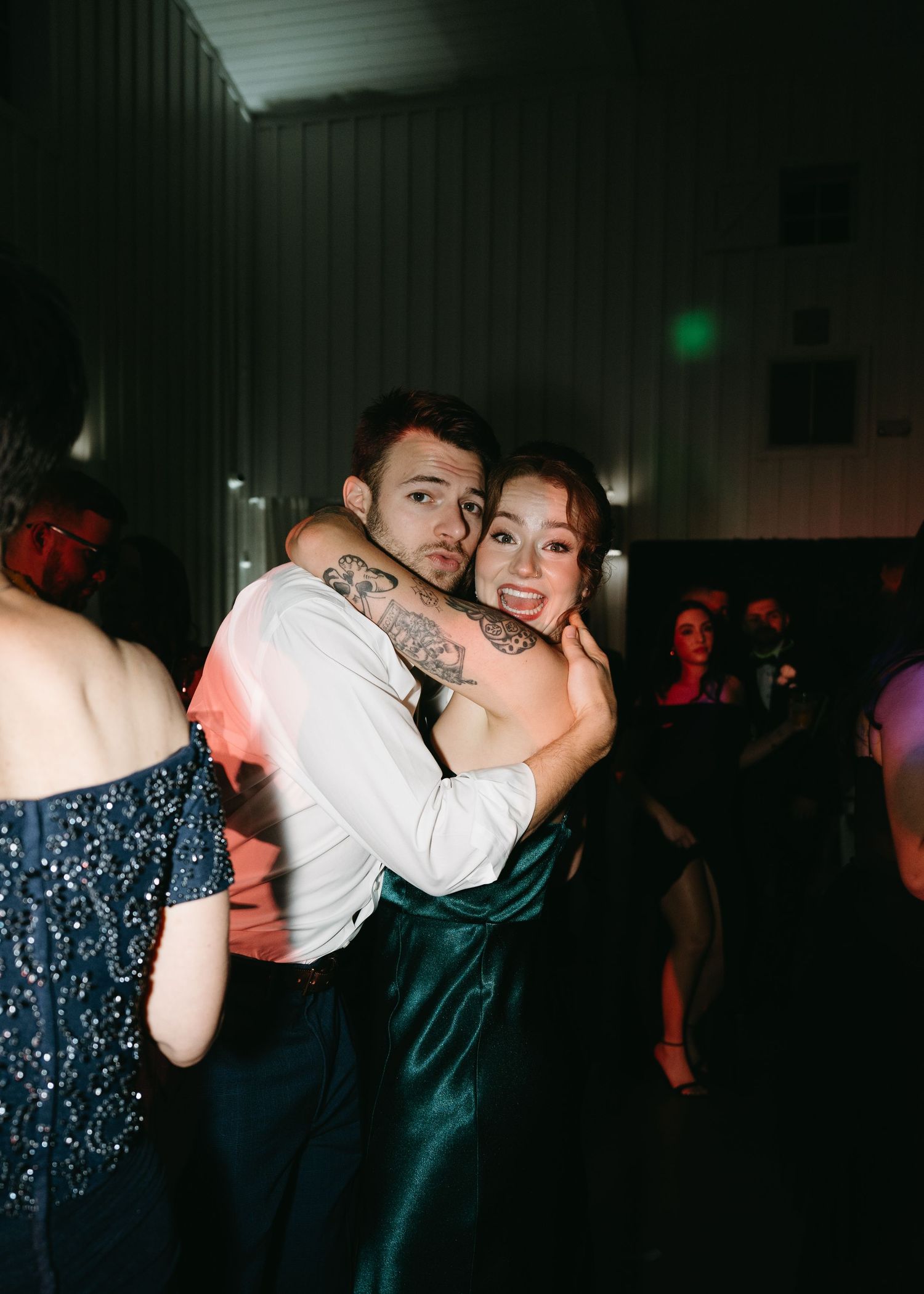 A couple dances together in a dimly lit room with colorful lighting creating a romantic atmosphere.