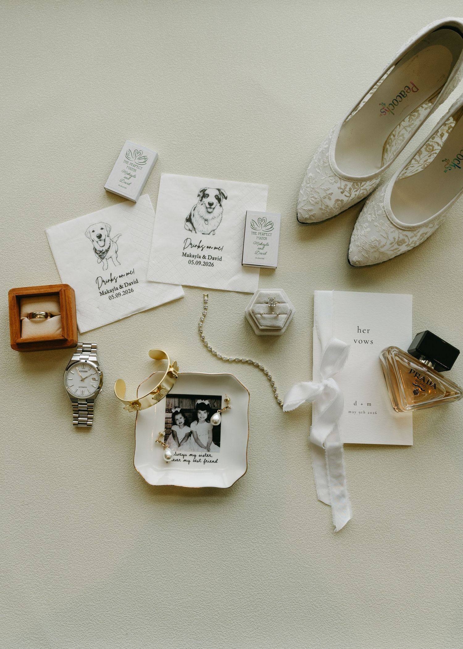 Elegant wedding flat lay with lace heels, gold ring, watch, perfume, vows booklet, pet portrait cards, and black-and-white photo frame.