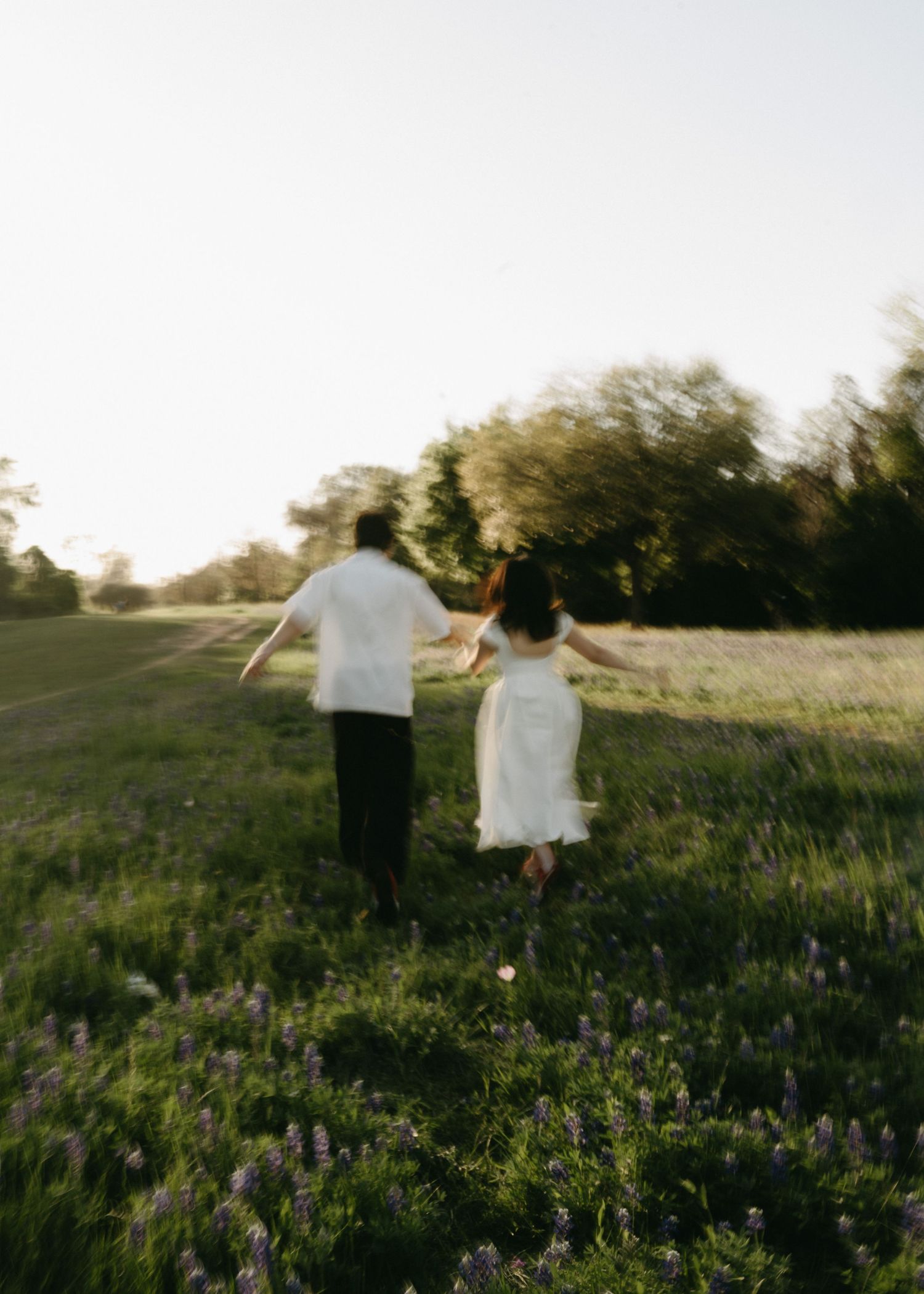 Two people walk through a wildflower meadow at sunset, their silhouettes backlit against the golden sky.
