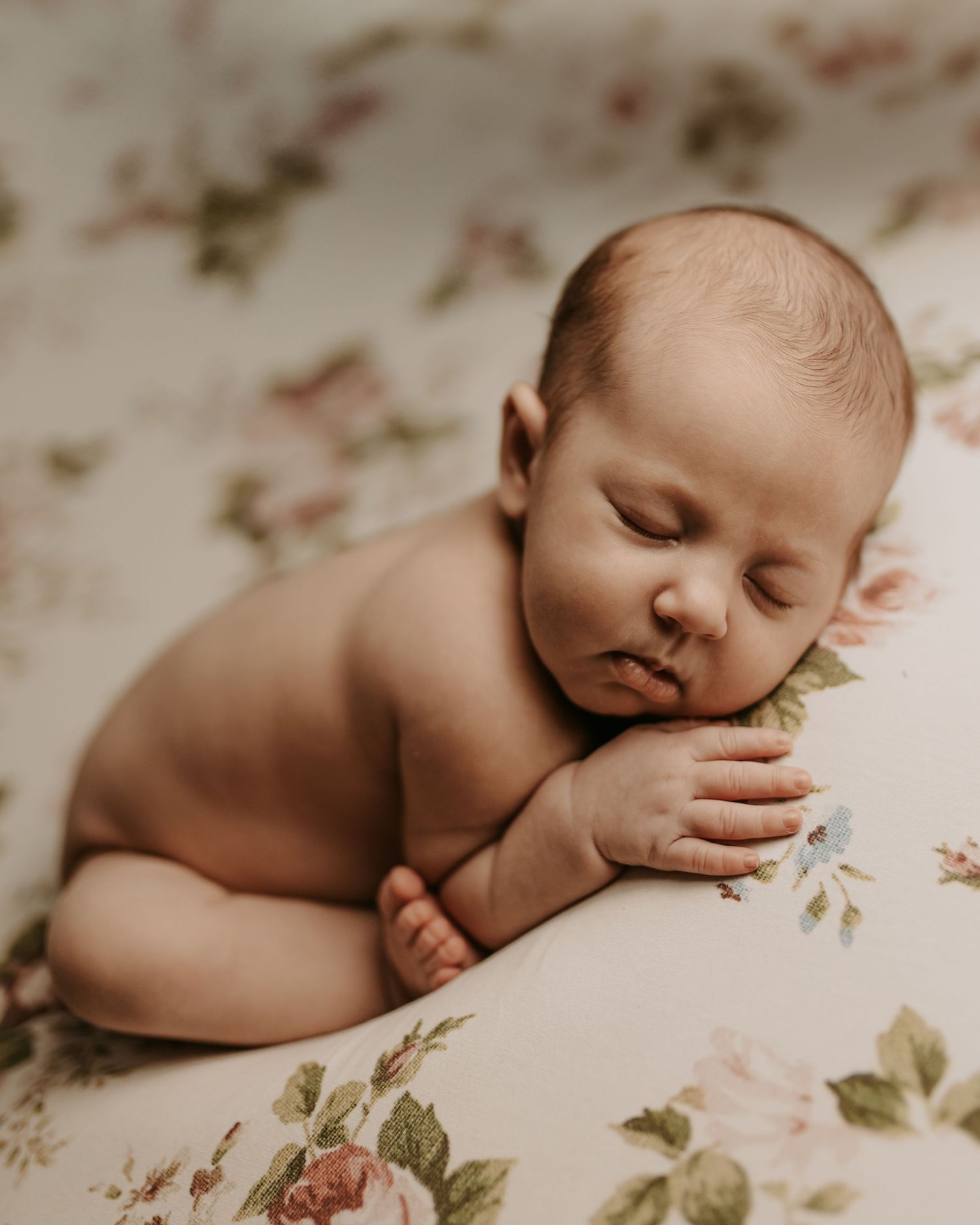 A sleeping baby lies peacefully on floral patterned fabric in soft, muted tones.