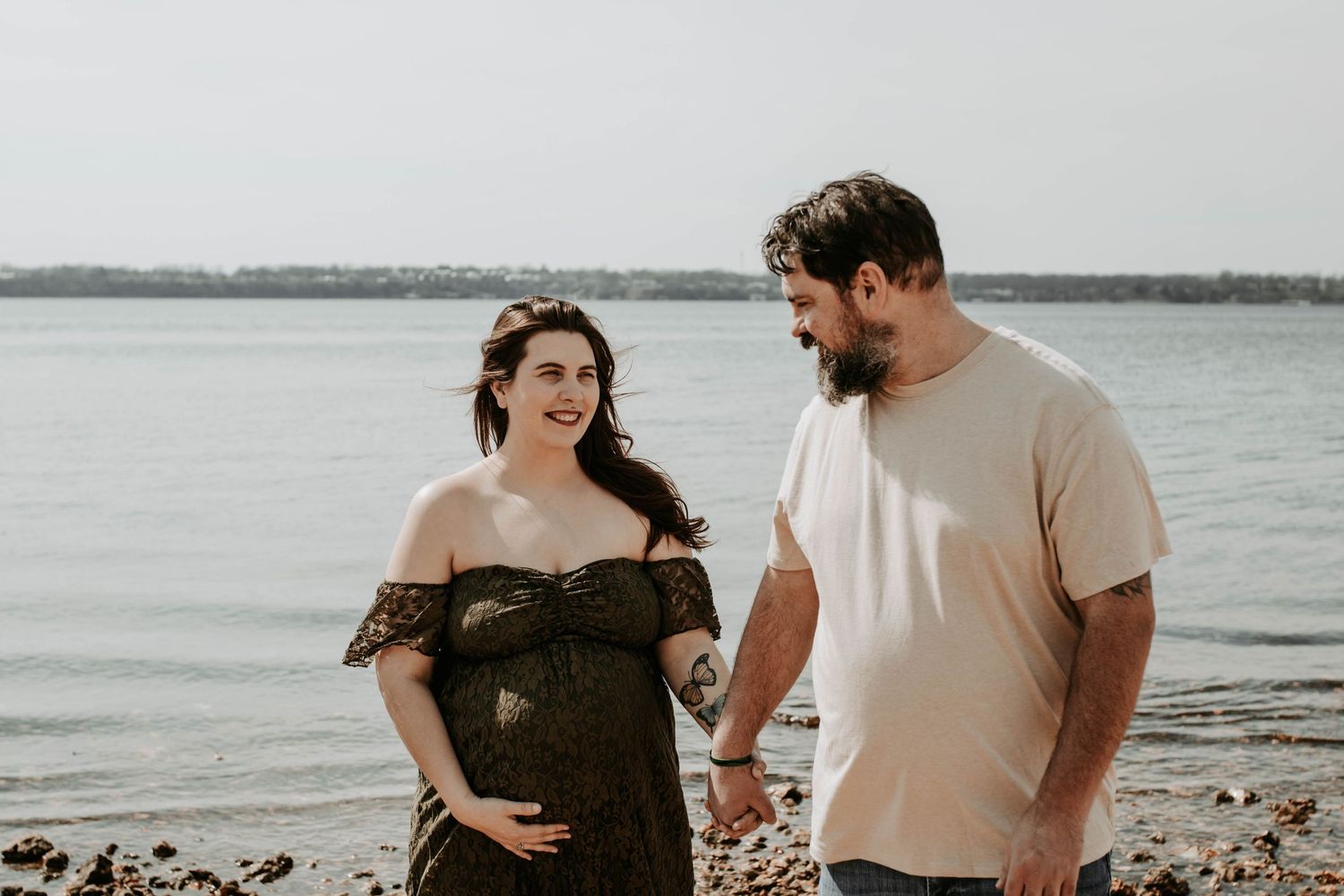 Expecting couple stands together on a beach during sunset in a casual romantic moment.