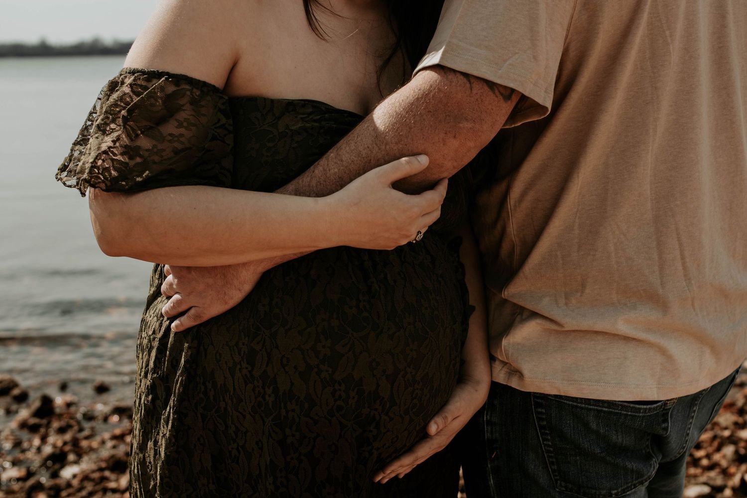 Close-up of pregnant woman's belly being embraced on rocky beach shore.