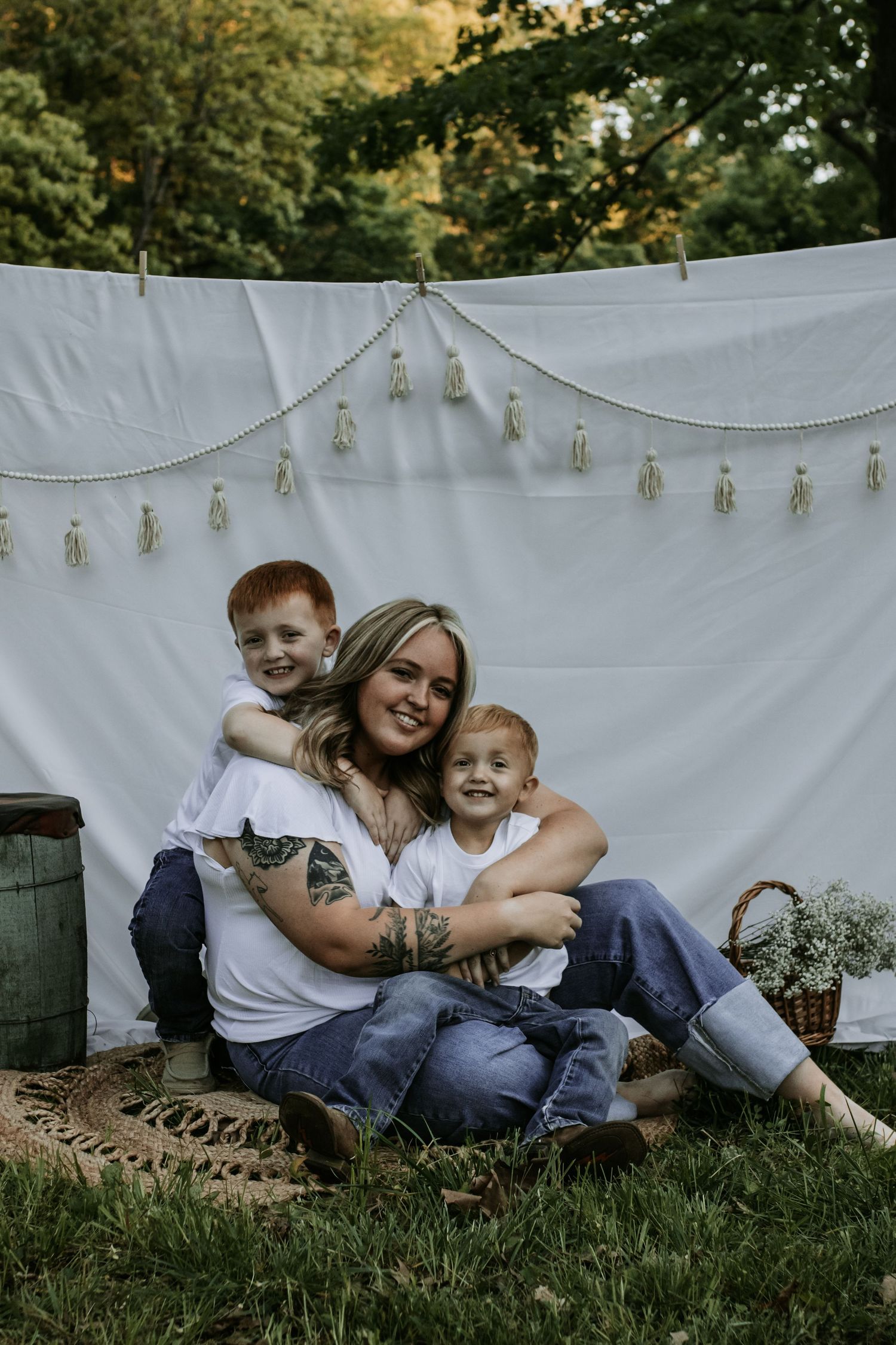 Outdoor family photo against white backdrop with string lights and natural greenery.