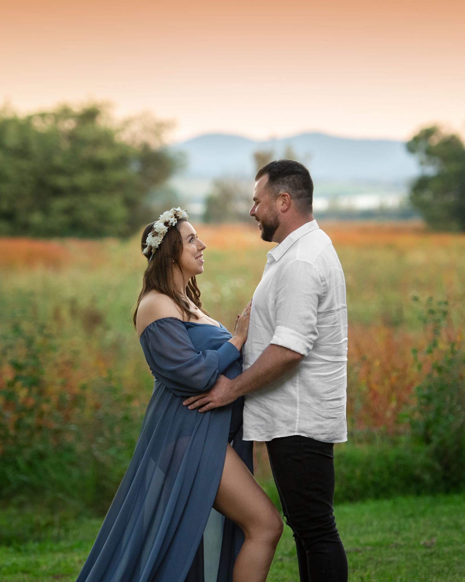 Intimate maternity session with couple embracing in field at sunset.