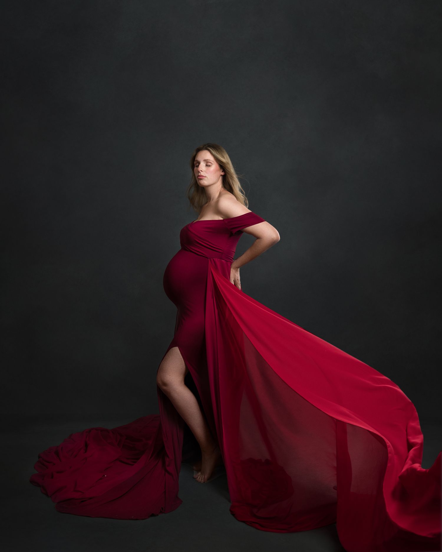 Dramatic red flowing dress against dark background creates striking silhouette in studio photography.