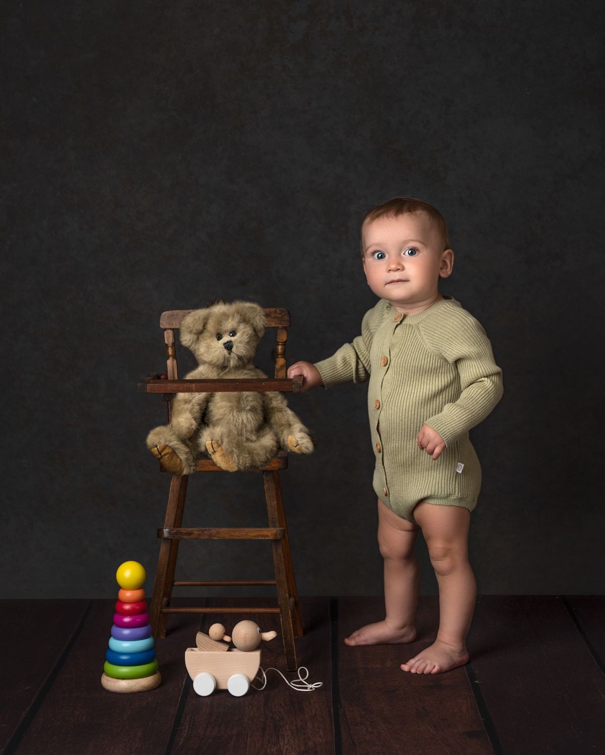 Wooden chair with teddy bear and colorful stacking toy against dark background.
