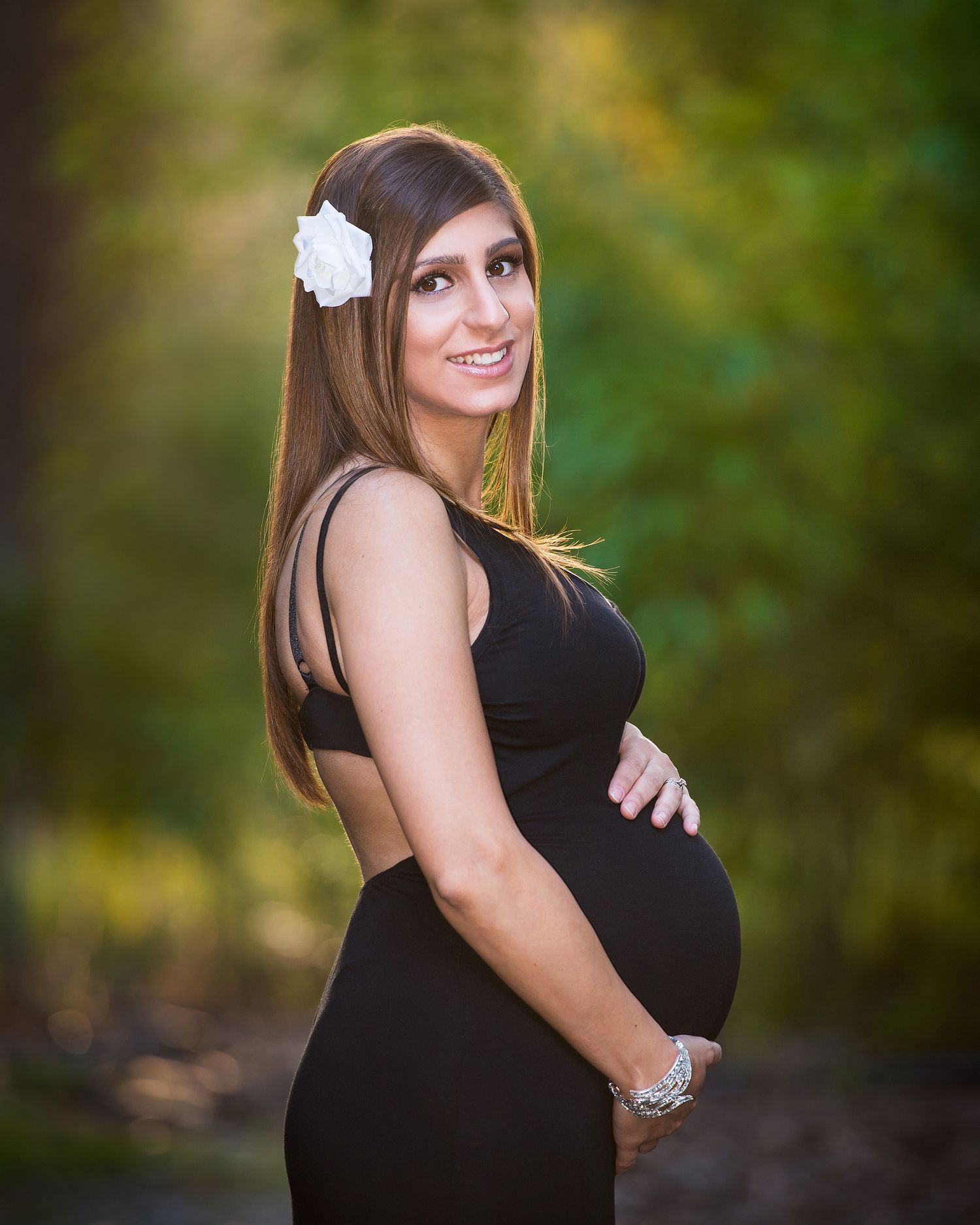 Outdoor maternity portrait session featuring black dress and natural greenery background.