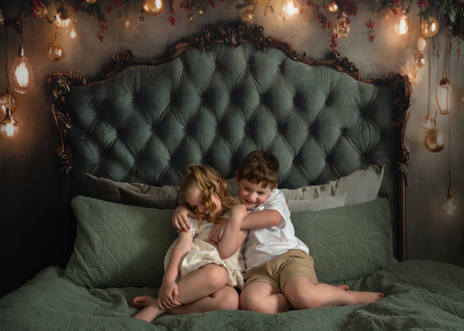 Siblings share sweet moments while lounging on an emerald green tufted sofa beneath glowing pendant lights.