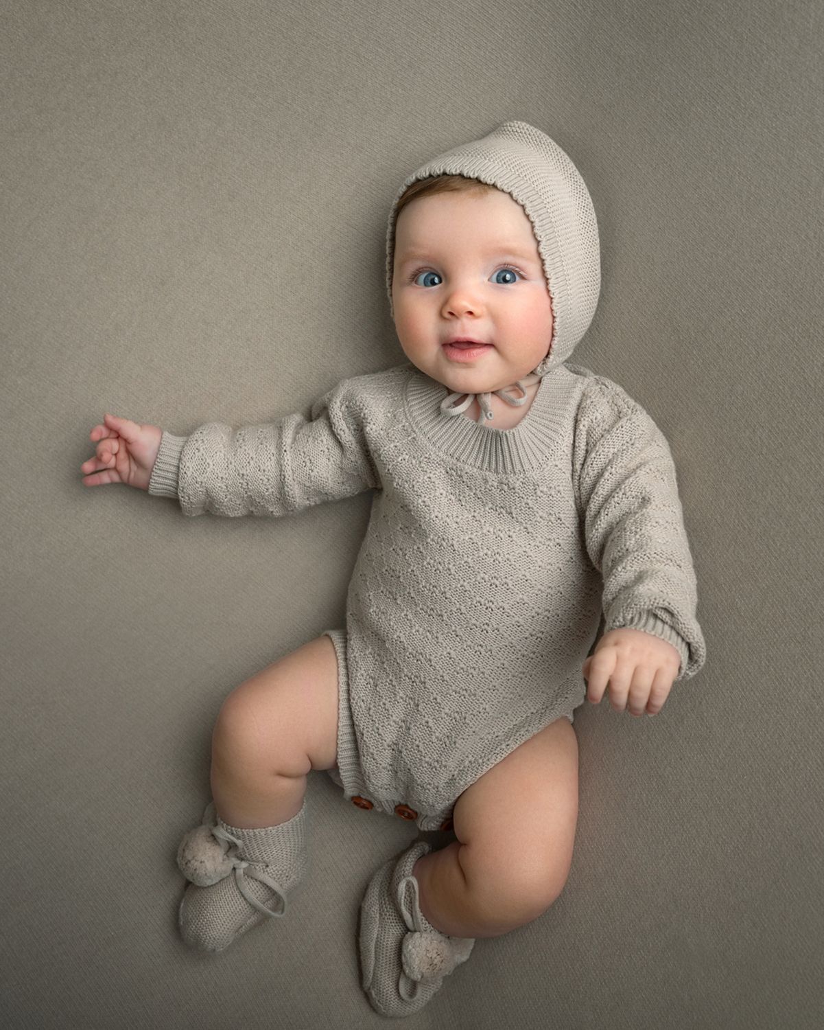 Baby wearing beige knit outfit photographed against neutral gray backdrop.