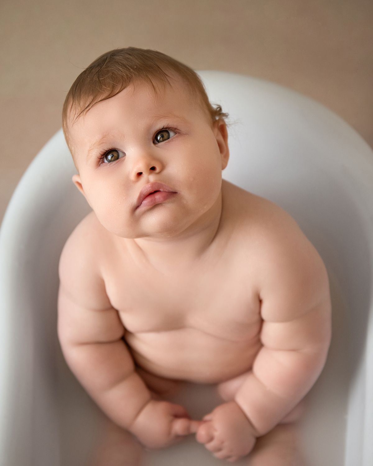 Baby sits in white chair during minimalist portrait session.