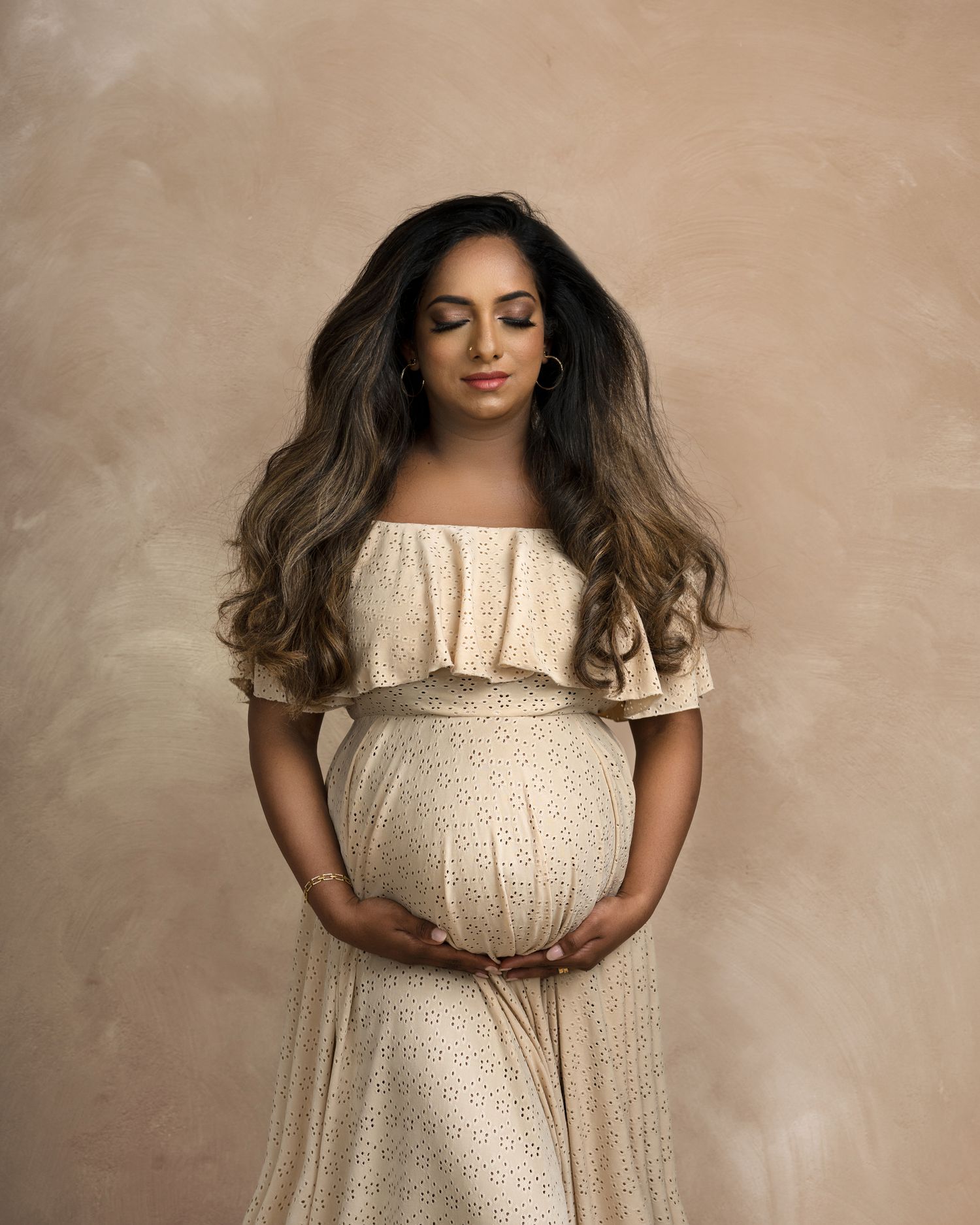 Cream colored lace maternity gown photographed against neutral beige background.