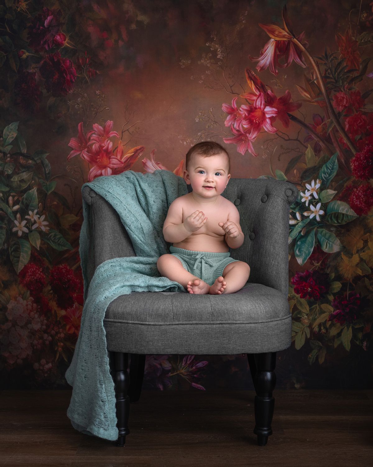 Vintage-style chaise lounge with teal blanket against floral wallpaper backdrop.