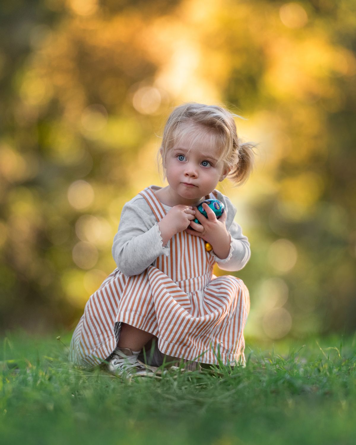 A child lies in grass during golden hour with warm autumn bokeh in background.